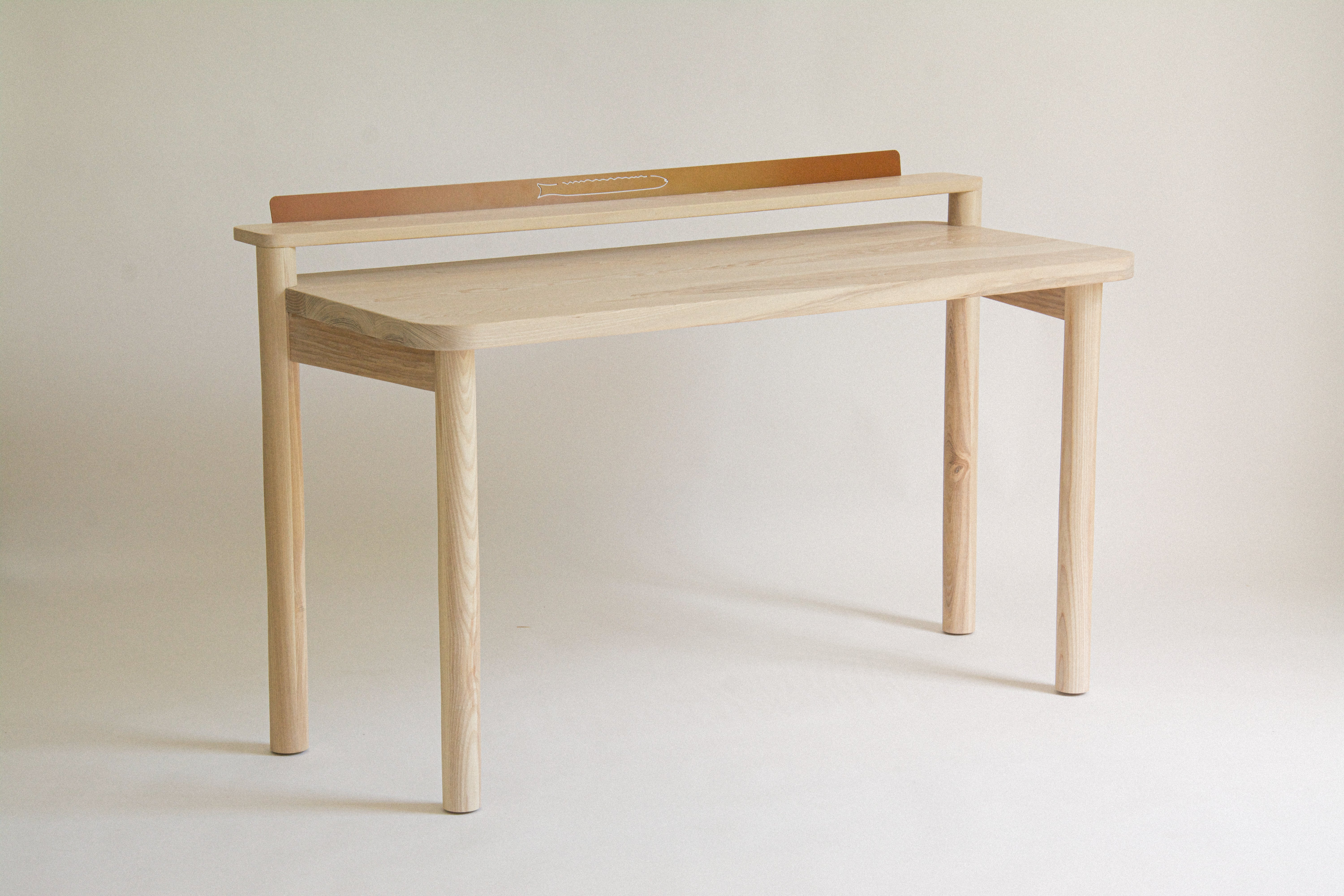 A solid ash desk of standard proportions, with an upper ledge made out of steel to be used to store postcards or assorted ephemera. 