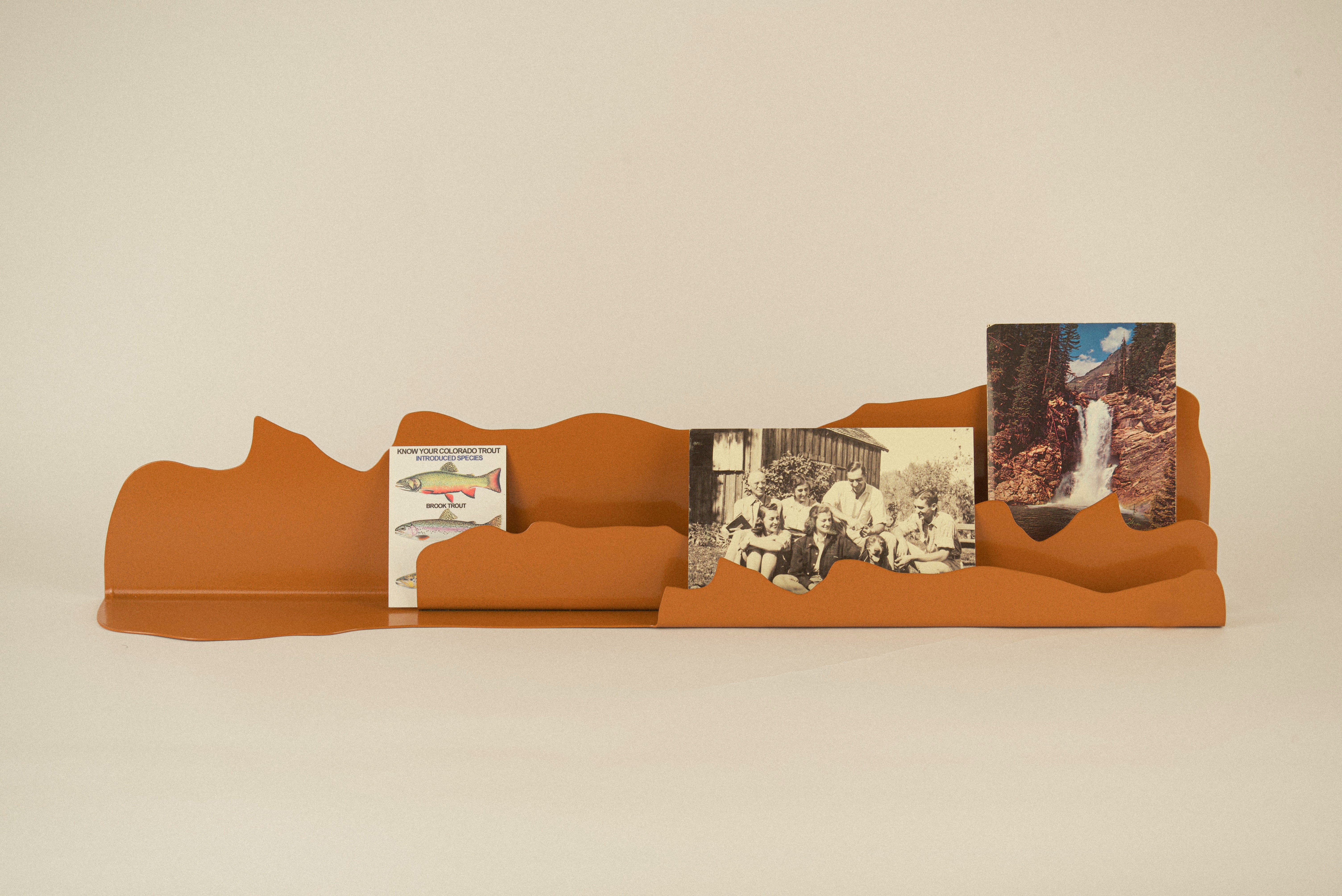 One burnt orange color steel shelf, showcasing three postcards.