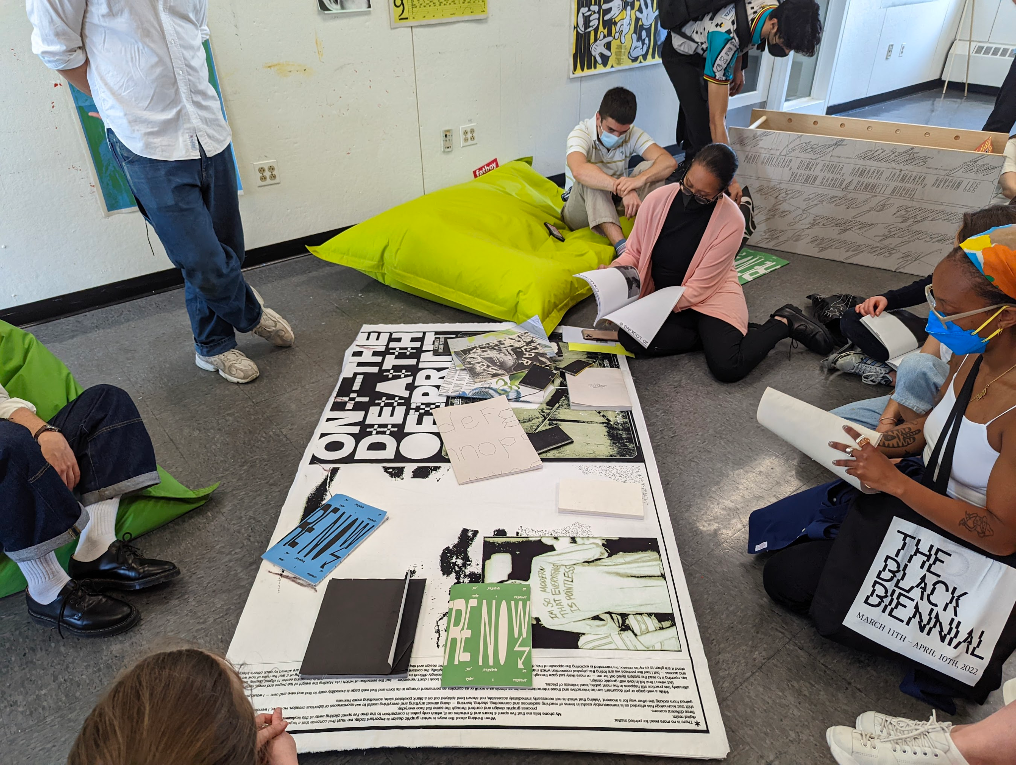 A group of people sit on the floor surrounding a poster covered by books