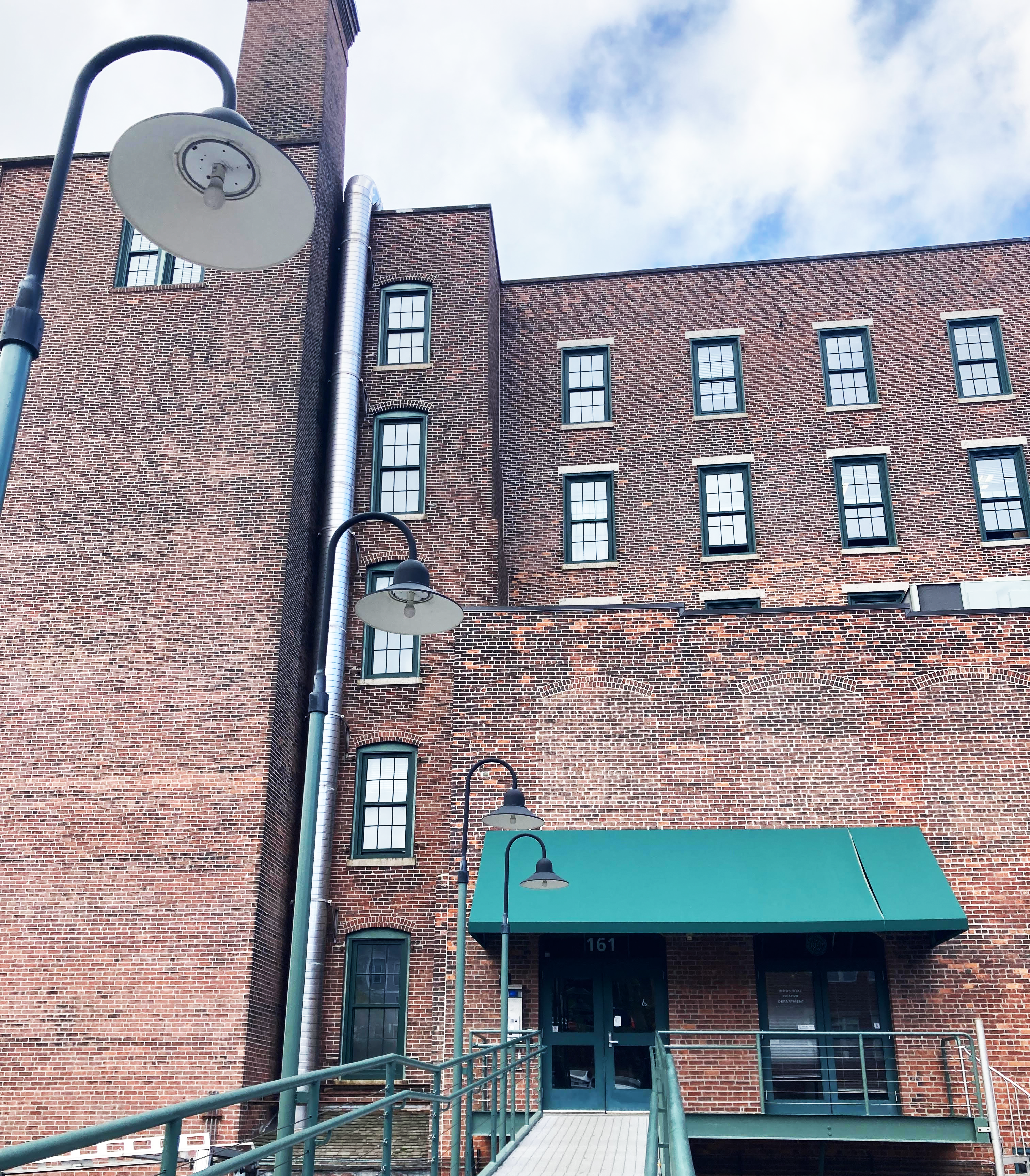 5 story brick building, viewed from the front as if walking up the ramp to its entrance. The entrance has a green awning.