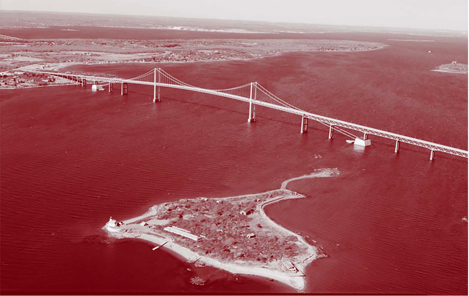 red-tinted aerial view of the Pell Bridge, a suspension bridge spanning a river with an island 