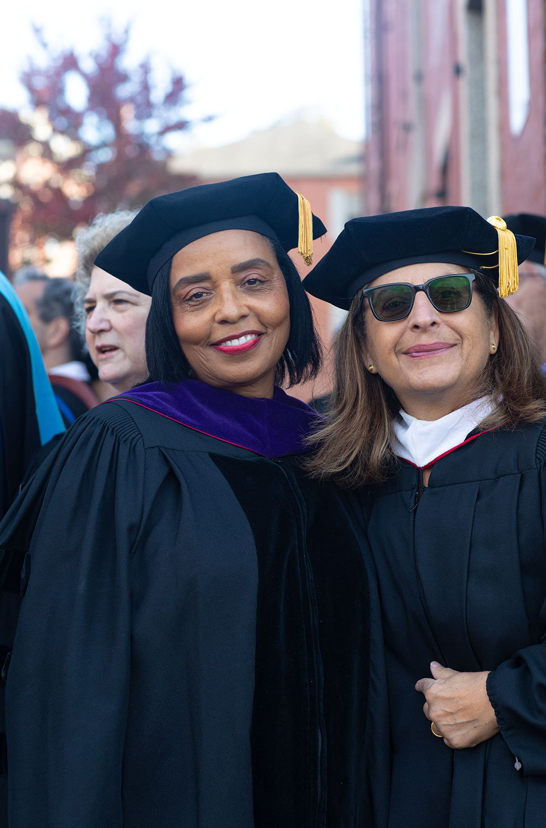 /A%20Black%20woman%20and%20a%20white%20woman%20in%20sunglasses%20stand%20in%20doctoral%20robes%2C%20smiling.