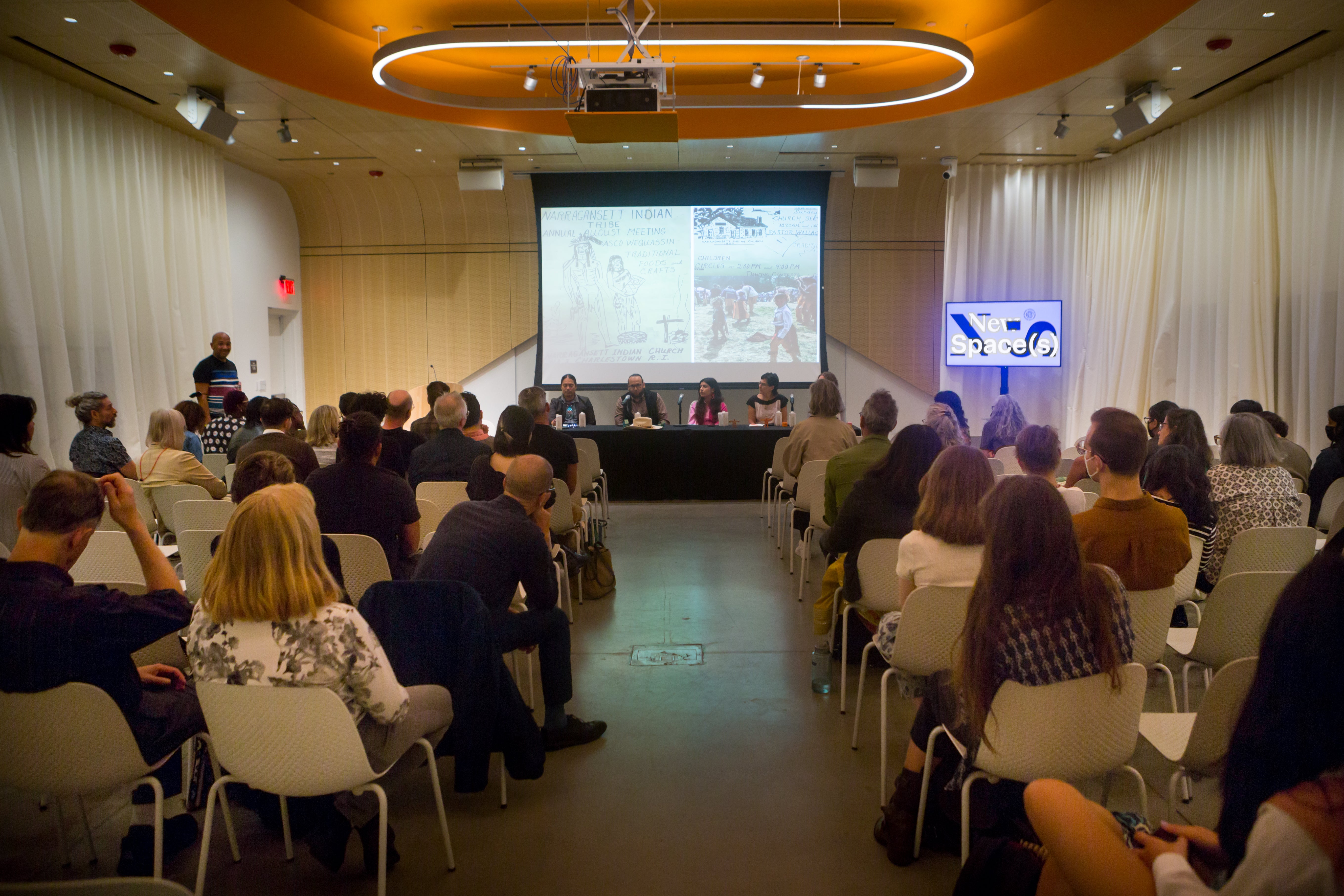 /Five%20panelists%20present%20to%20a%20crowded%20audience.%20The%20projector%20behind%20them%20shows%20a%20drawing%20with%20handwritten%20text%20reading%20%27Narragansett%20Indian%20Tribe%20Annual%20August%20Meeting%27