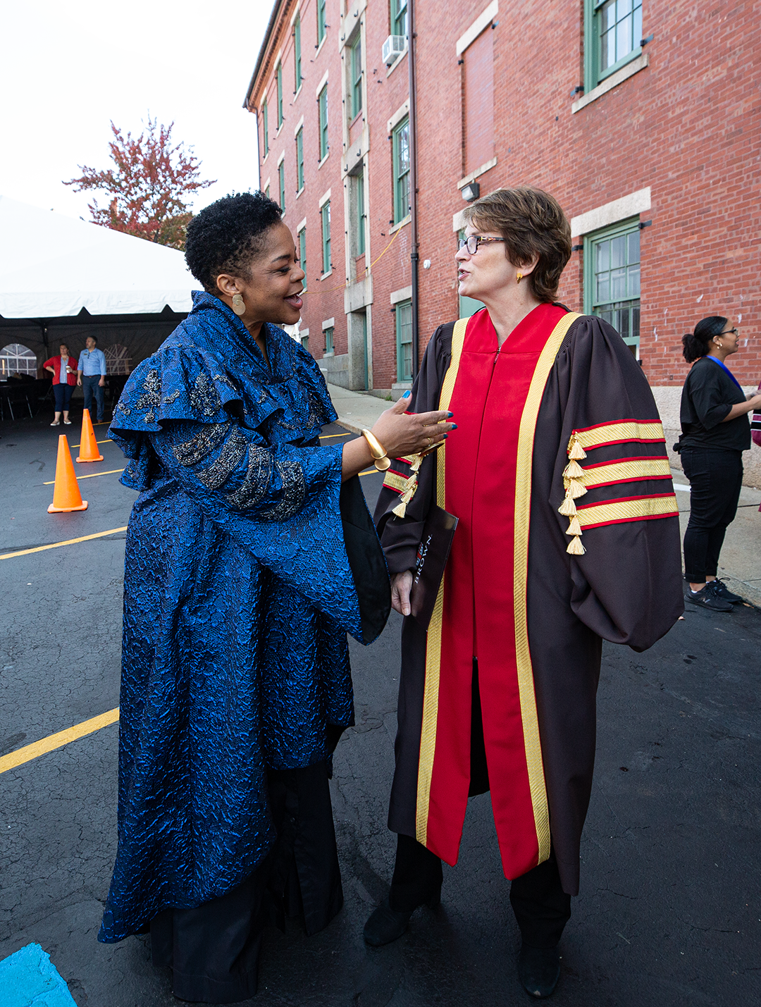/A%20Black%20woman%20in%20blue%20ceremonial%20robes%20engages%20in%20cheerful%20conversation%20with%20a%20white%20woman%20in%20doctoral%20robes%20with%20red%20and%20golds%20stripes.