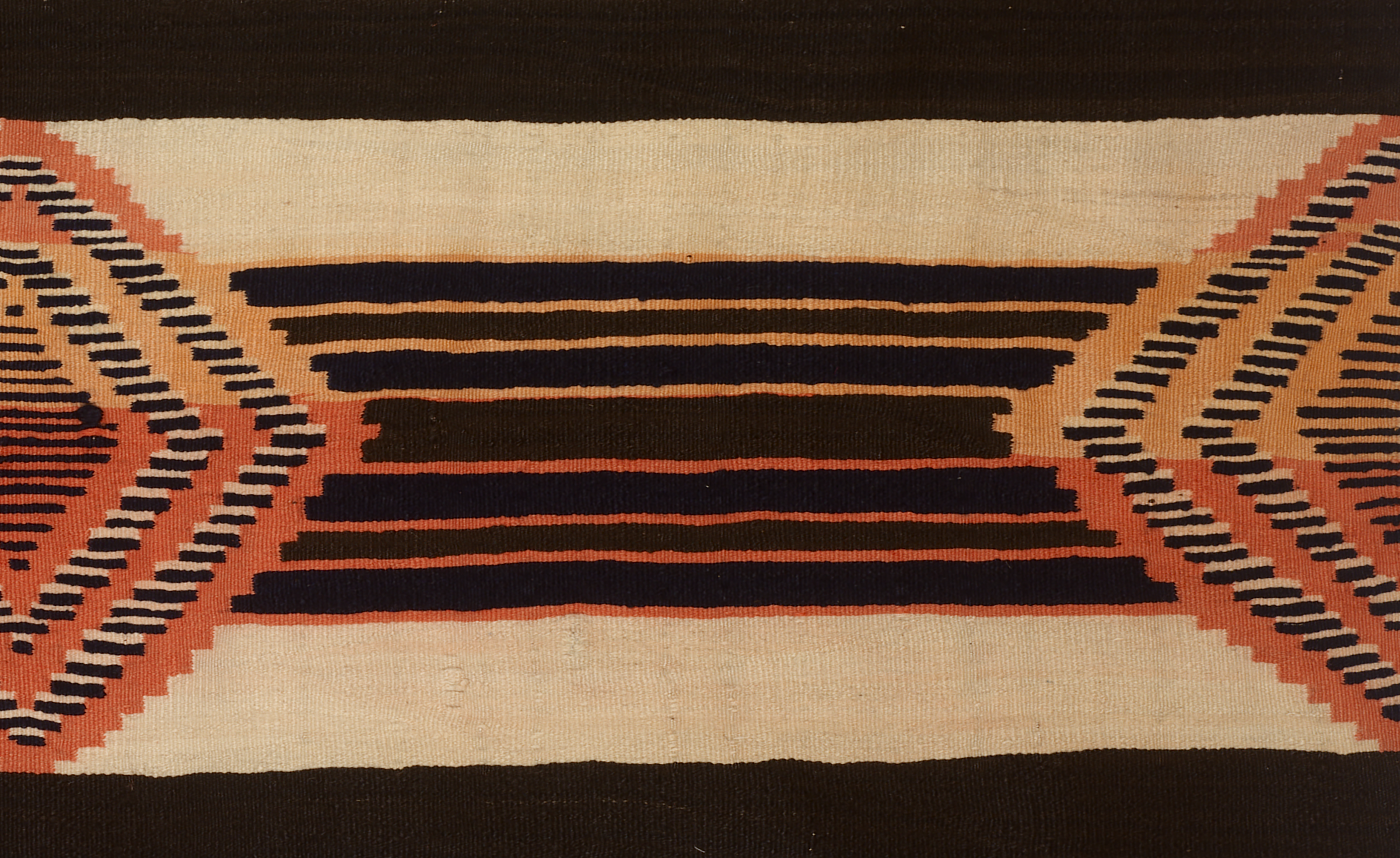 A woven textile with black and orange stripes of various sizes and shapes on a tan colored background. 