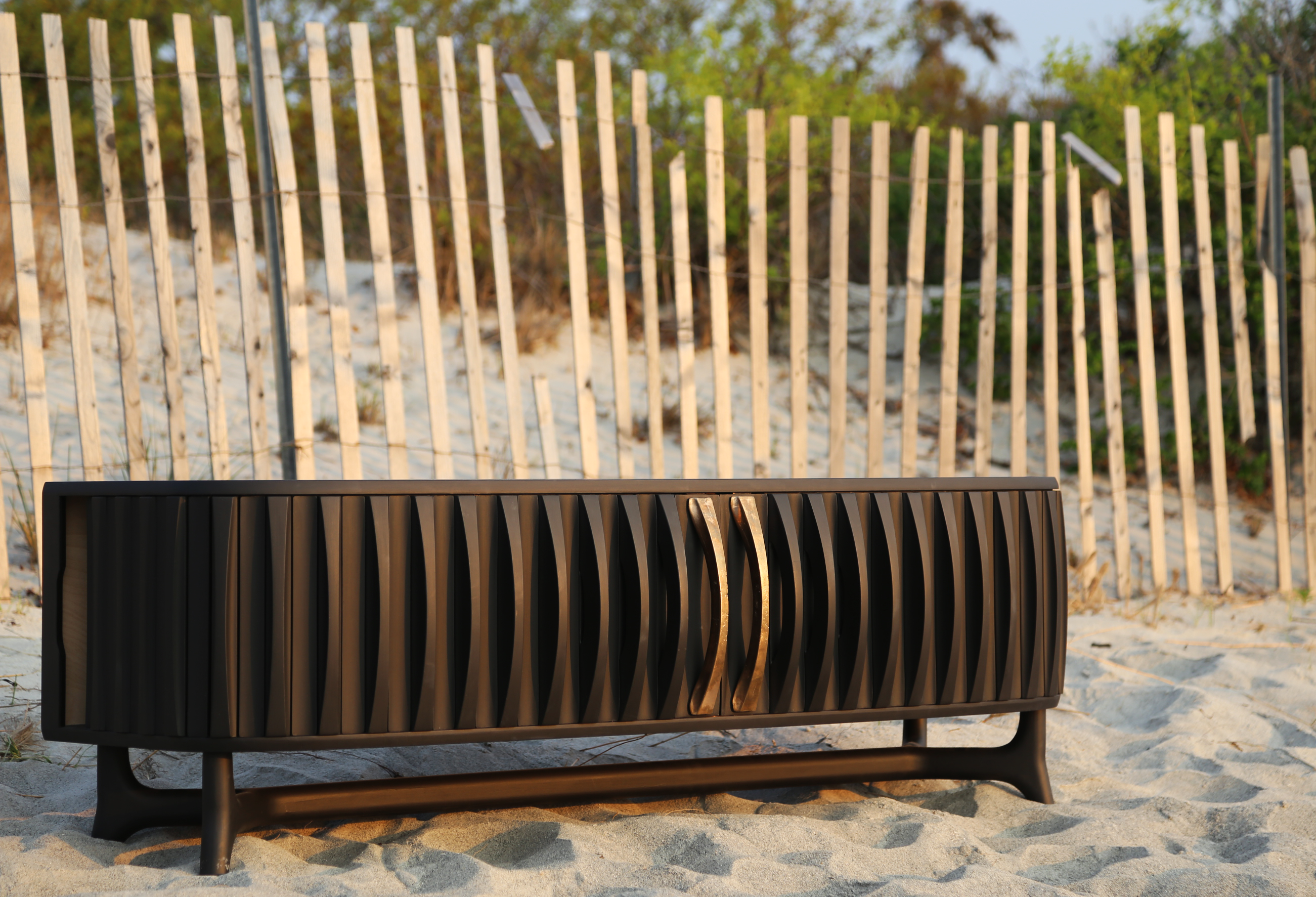 Black media cabinet with bronze handles on beach