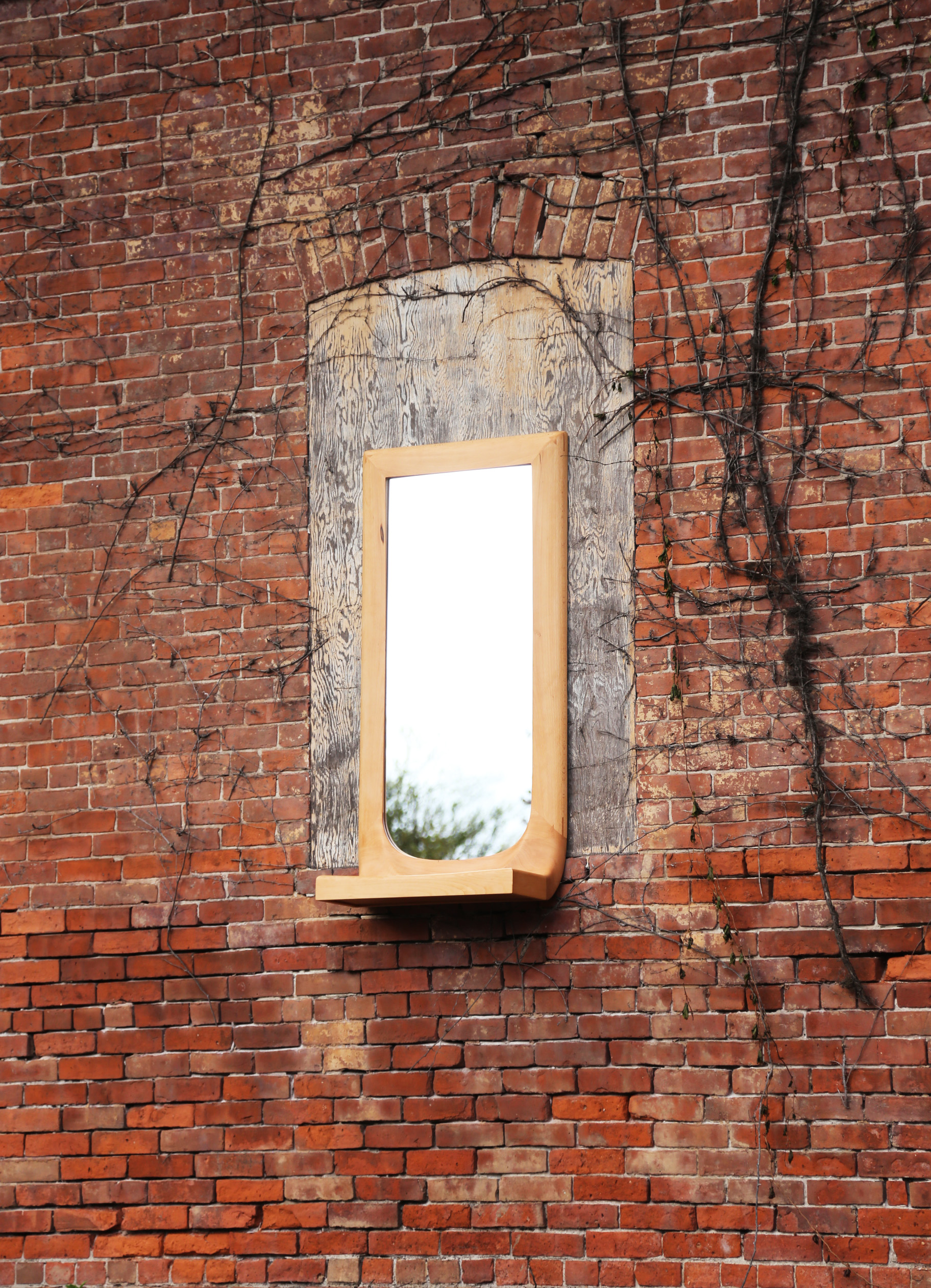 Beech wood mirror with integrated shelf on brick background