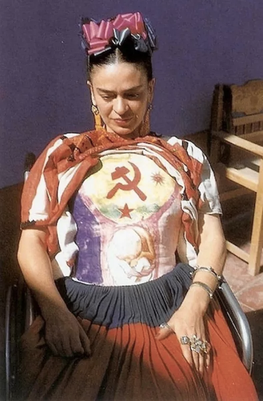 Photograph of Frida Kahlo seated in a wheelchair wearing a cast that has a hammer and sickle painted on it