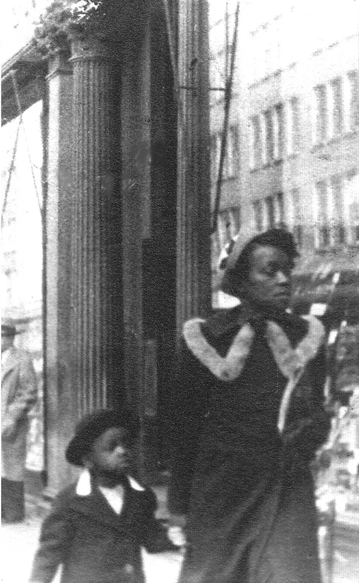 Black and white photograph of a small girl holding her mother's hand as they walk down the street