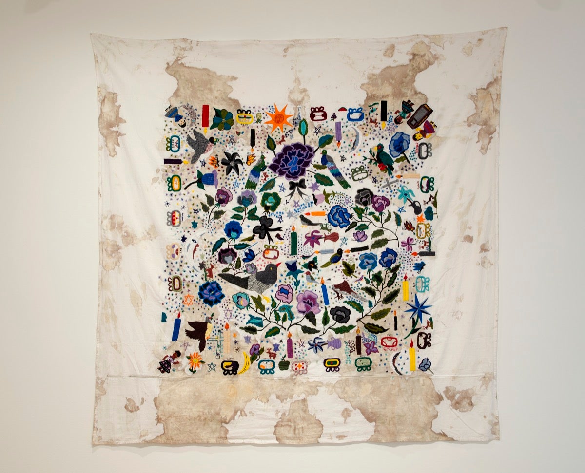 A cloth stained with blood and multiple colorful embroidered flora and fauna atop.