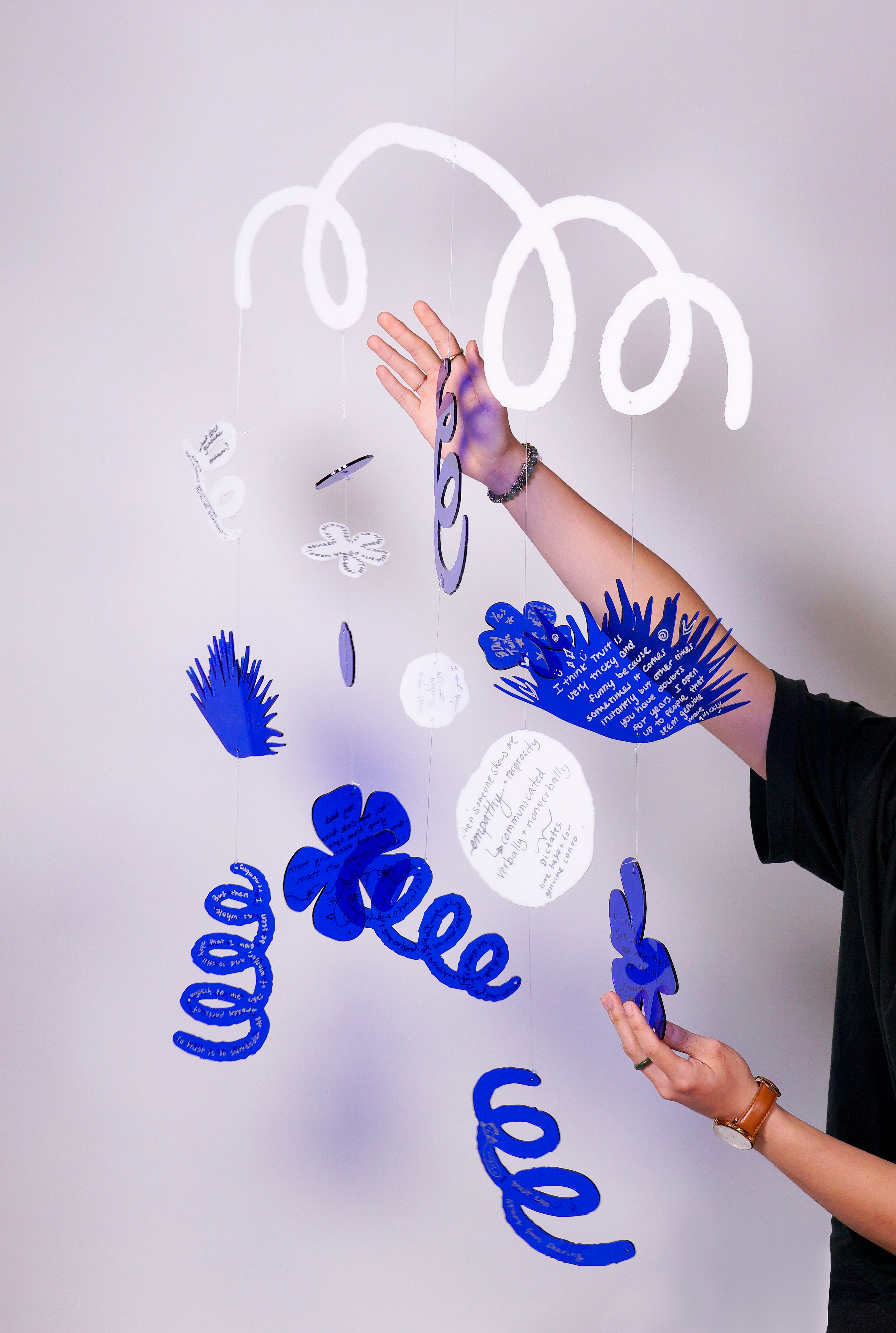 A mobile with transparent blue and white plexiglass cut in shapes of flowers and plants.