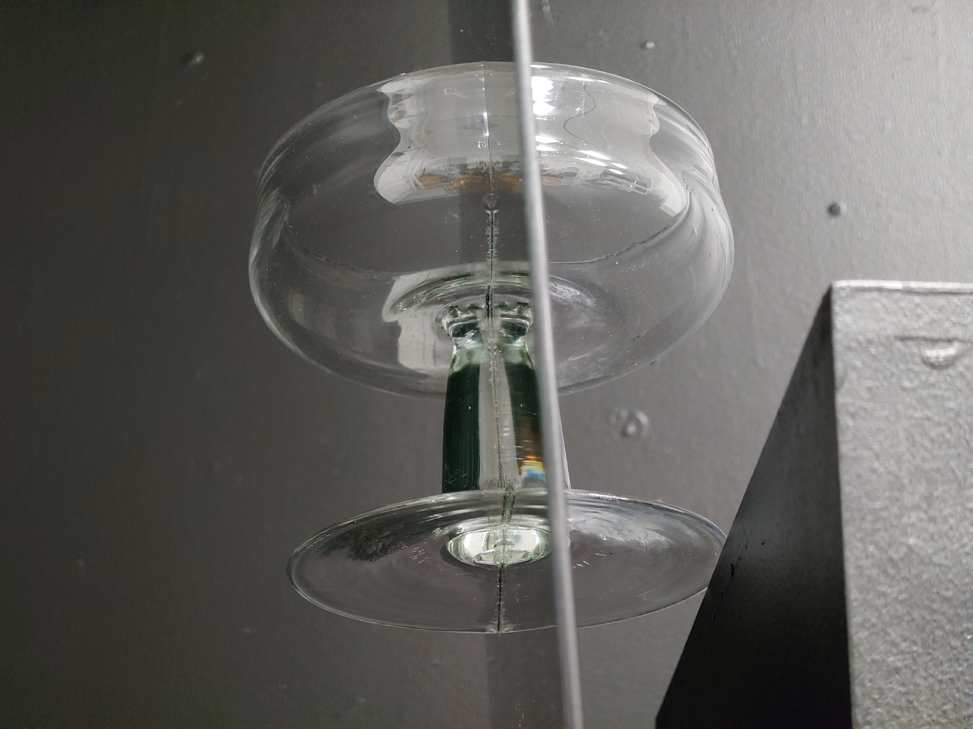 Halves of a hand-blown goblet glued onto each side of a mirror and resting meticulously at the edge of a pedestal.