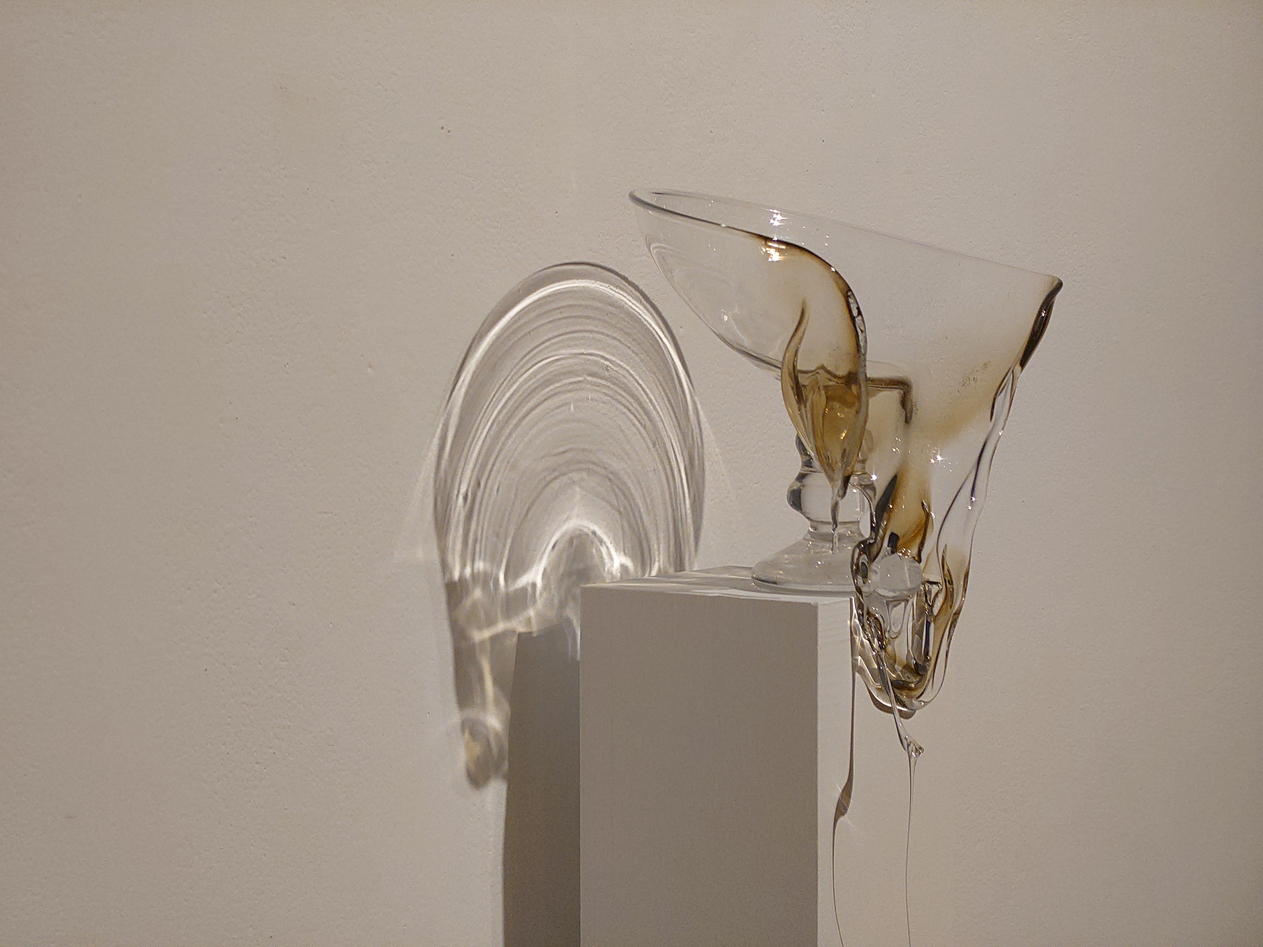 A slumped hand-blown goblet receiving a spotlight, casting a haloed shadow on the wall.