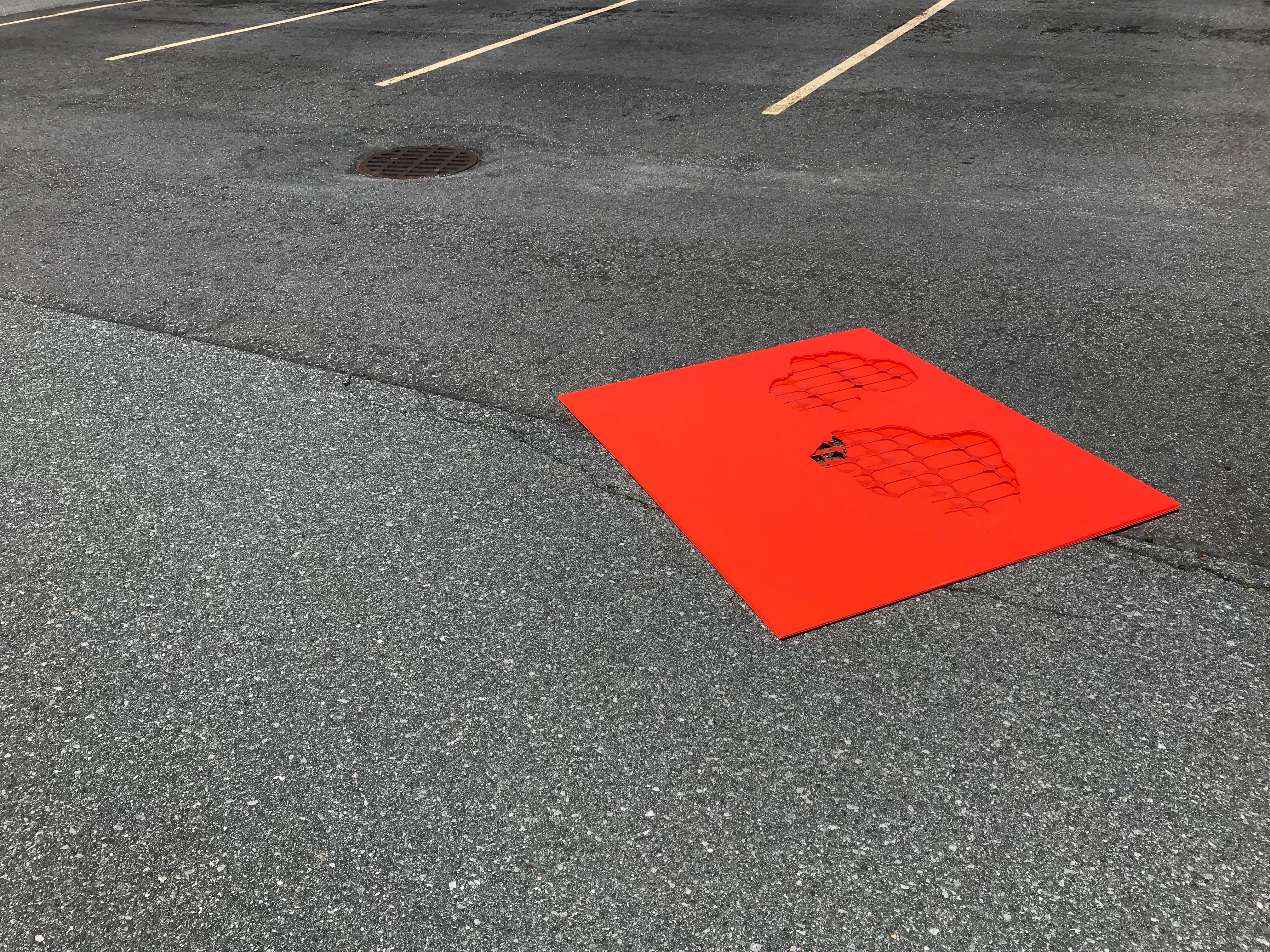 A flat orange plastic rectangle with cut-outs lays on the asphalt of an empty parking lot.