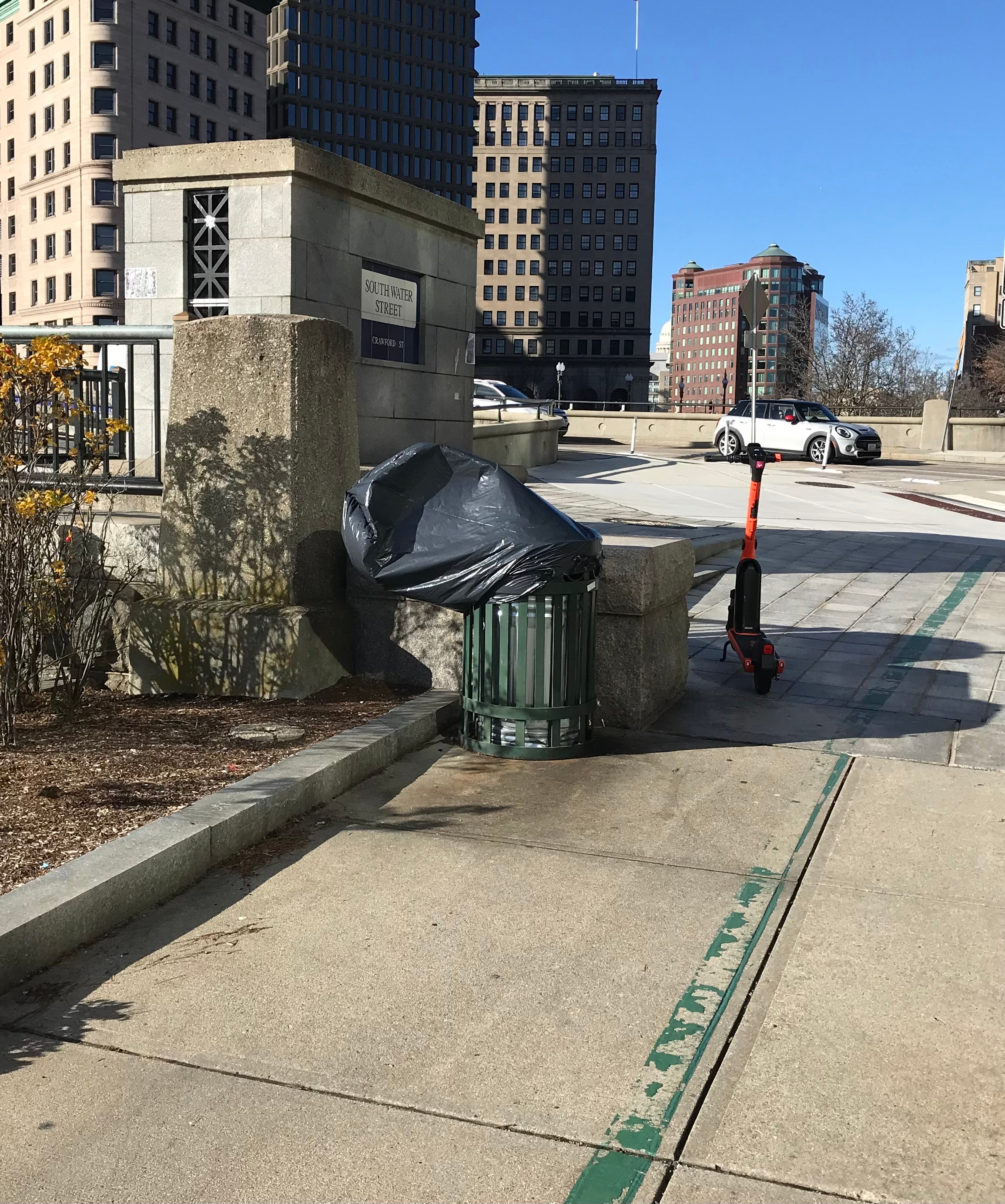 A trash can along the Providence River with the bag blowing around above the can in the wind.