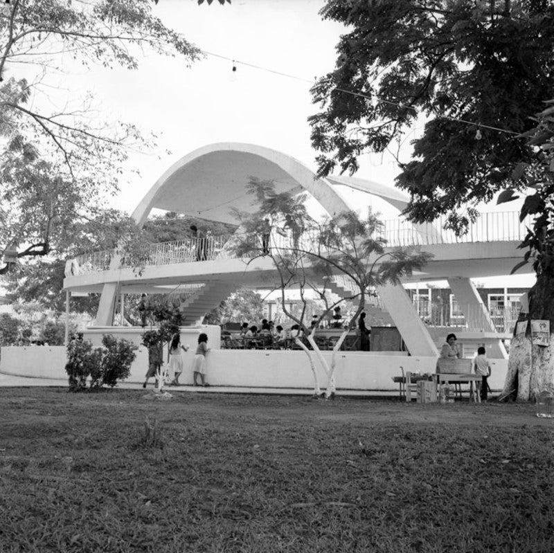 A group of children play underneath an arched, Modernist pavillion. 