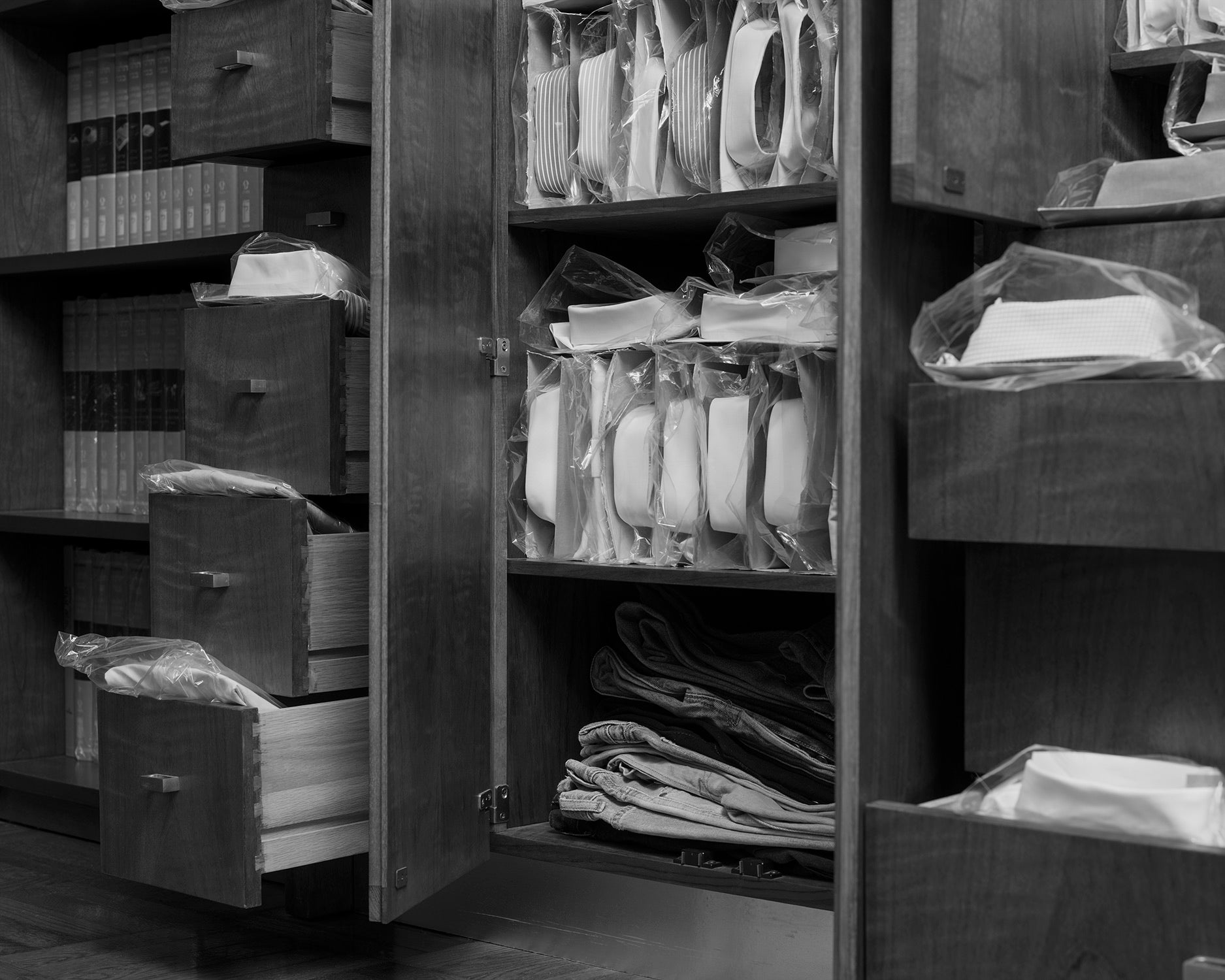 Black and white pigment print of folded shirts emerging from cabinets and drawers. 