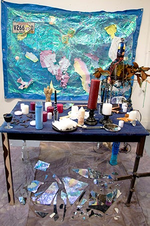 Table with painting and wall piece along with chair sculpture modeled after figure.
