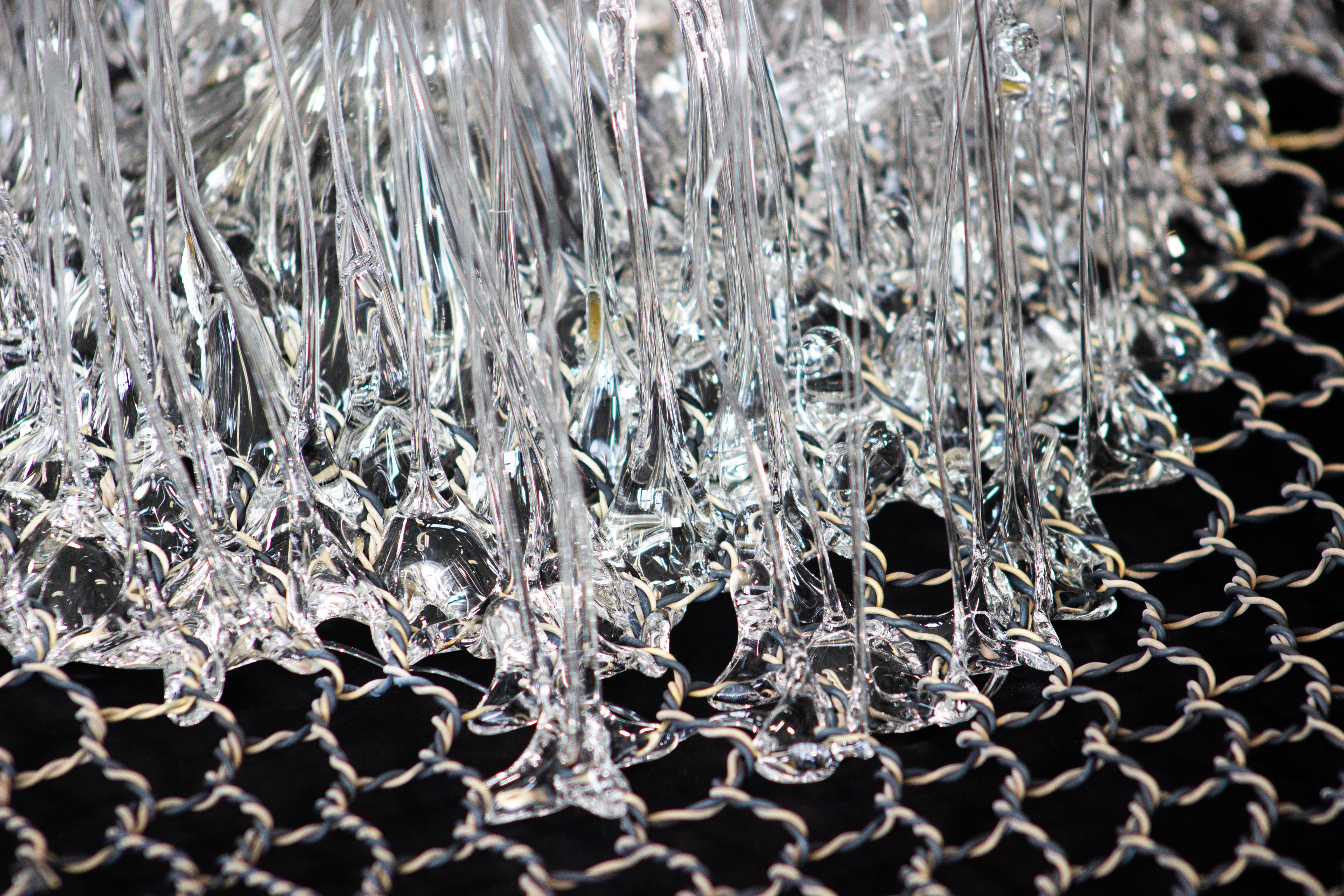 Piece of a hand-woven chicken-wire fence with molten glass coming through its holes.