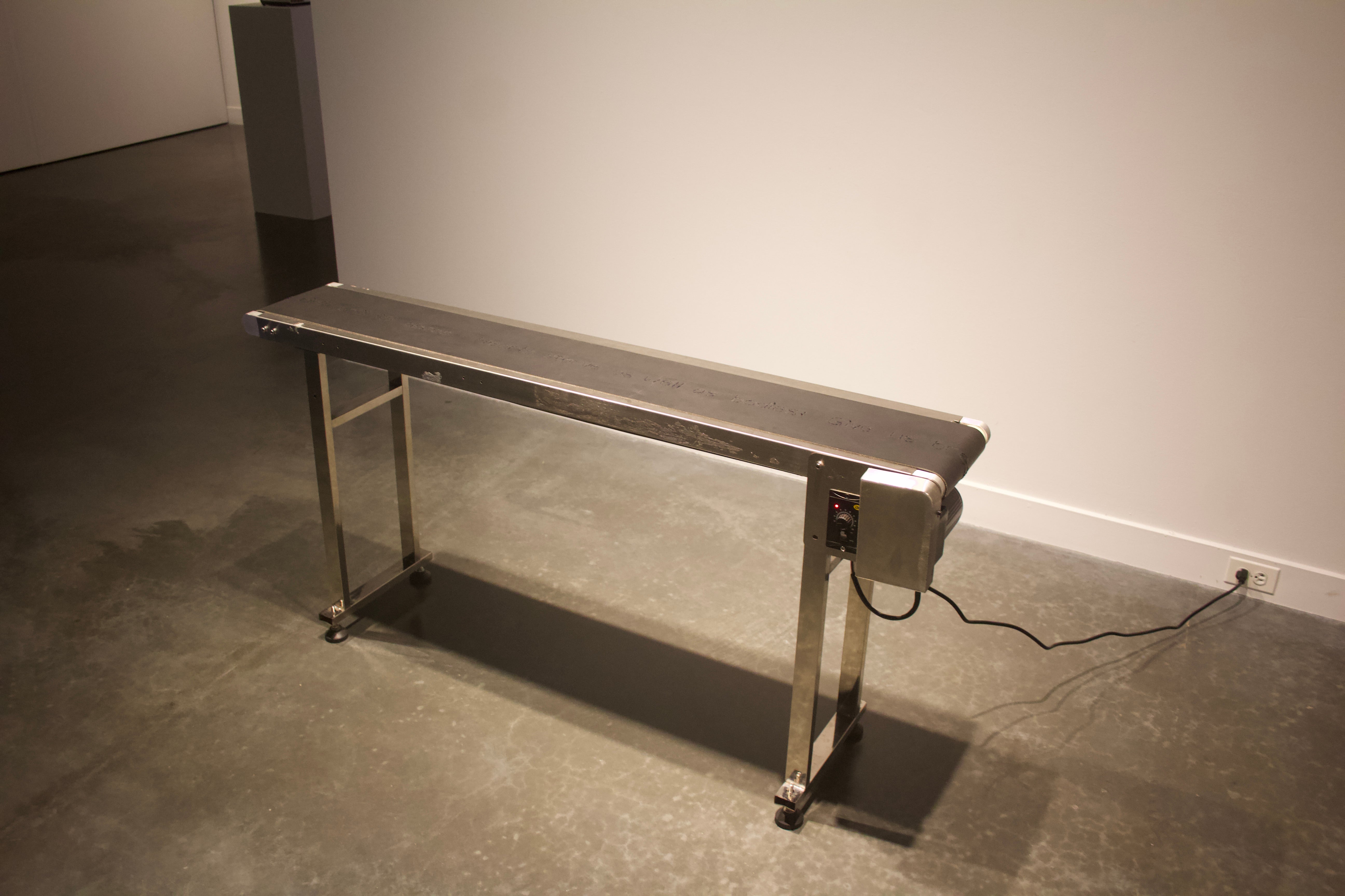 The rubber of a conveyor belt is embroidered with a poem that reads: "Our days shall not be sweated from birth until life closes; hearts starve as well as bodies, give us bread but give us roses." 