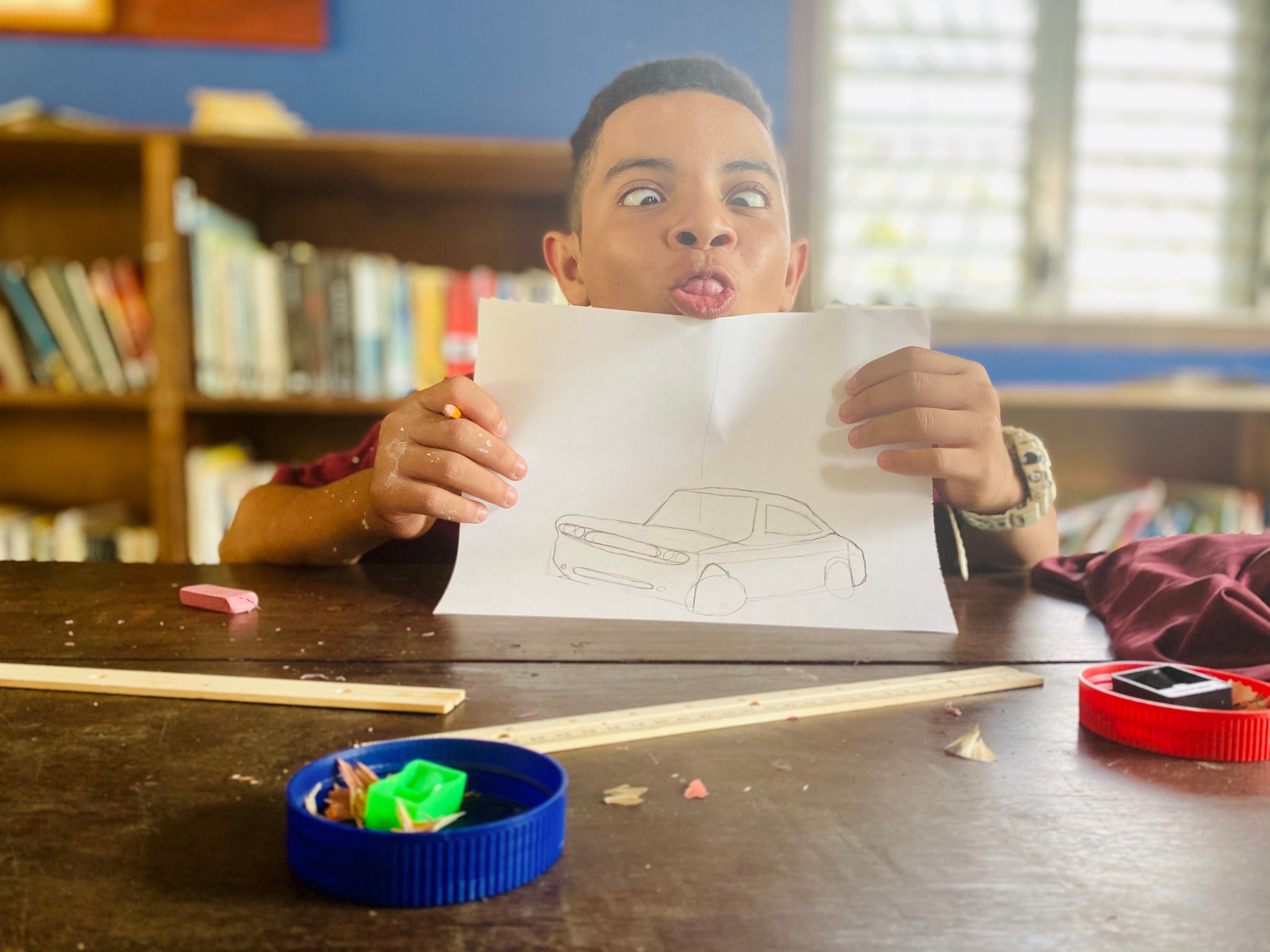 Middle school student holding pencil drawing of a car and making a silly face.