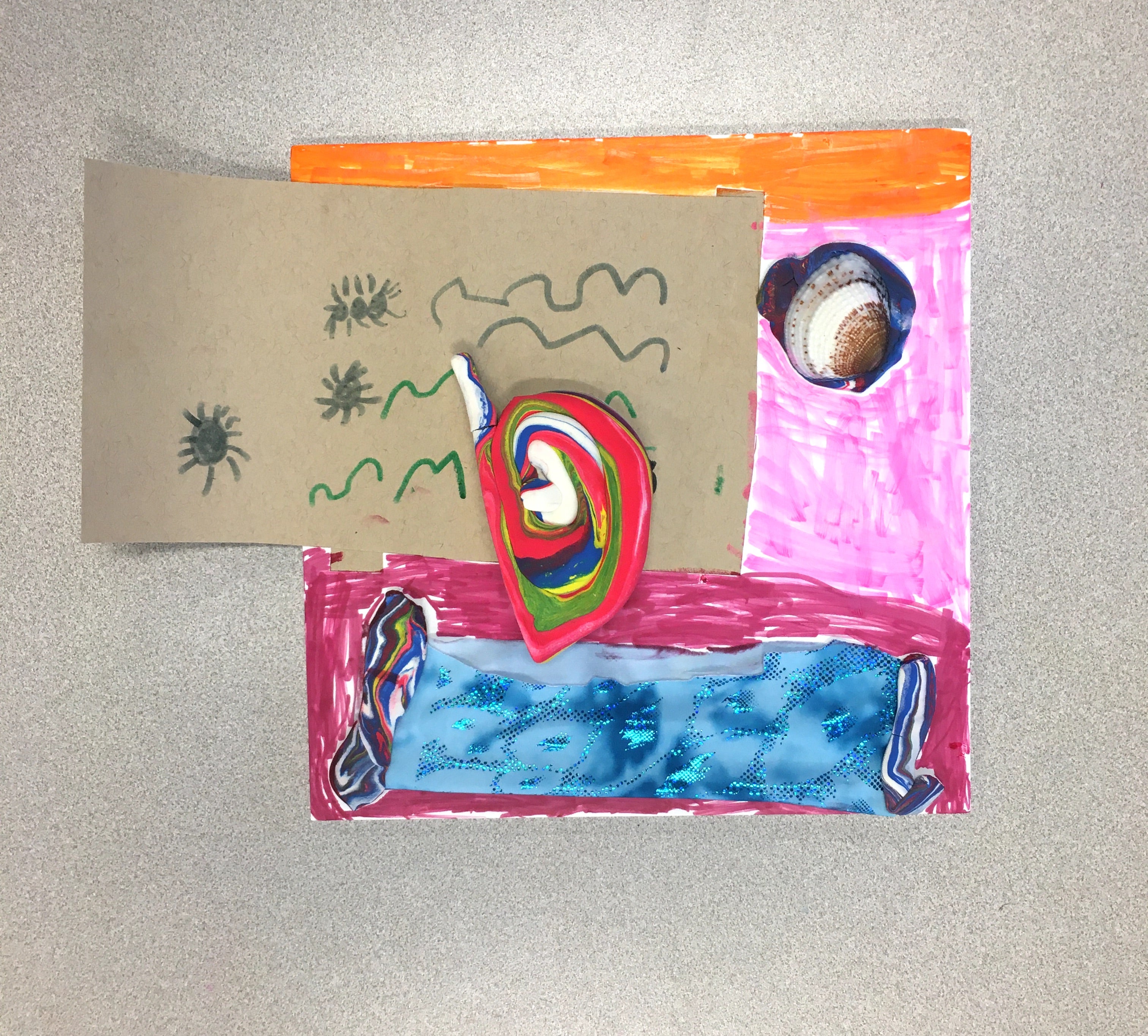 A square piece of white foam core colored with marker in sections of orange, pink, and pinkish red. A shell is attached to the pink section, sitting on a blob of dark blue and red air-dry clay. A sparkly blue piece of stretch fabric is affixed to the pinkish red section with two strips of color-swirled air-dry clay on either end of the fabric. A rectangular piece of cardboard covers a large portion of the foam core and extends beyond the left side. The cardboard has squiggly lines and insects drawn on it in