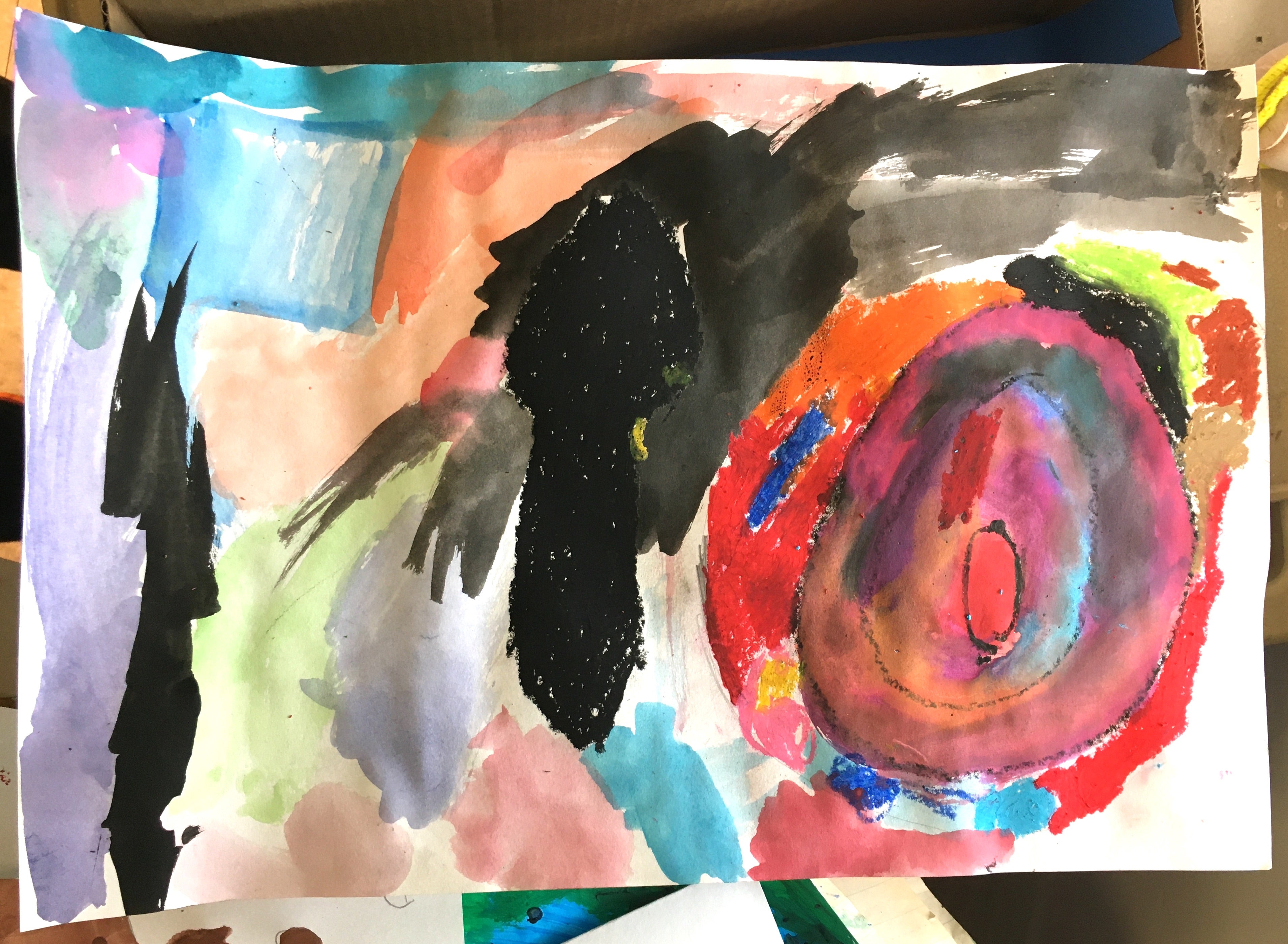 An in progress artwork of a wide black spoon drawn in oil pastel next to a plate drawn with oil pastel and filled in with pink watercolor with other hues blended in. Colored splotches of oil pastel are circling the edges of plate and the rest of the page is filled with wispy watercolor except the bottom right corner which is left white for now.