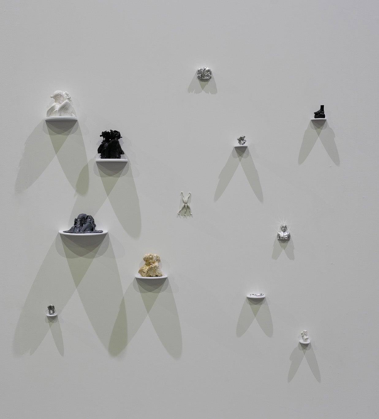 A grouping of sculptures of various materials sitting on individual shelves