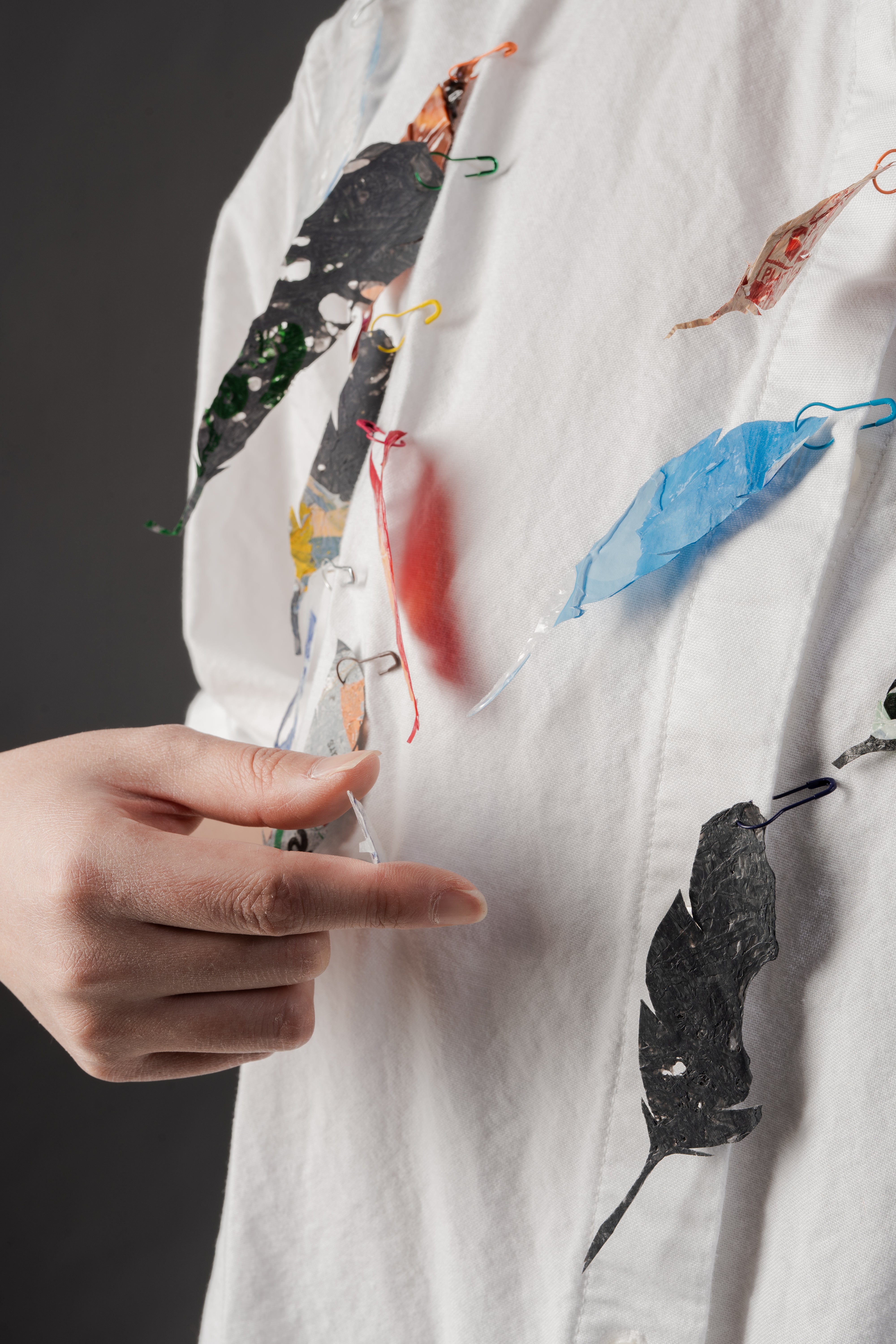 A photo of a model wearing feather brooches, with a hand appearing in the photo.