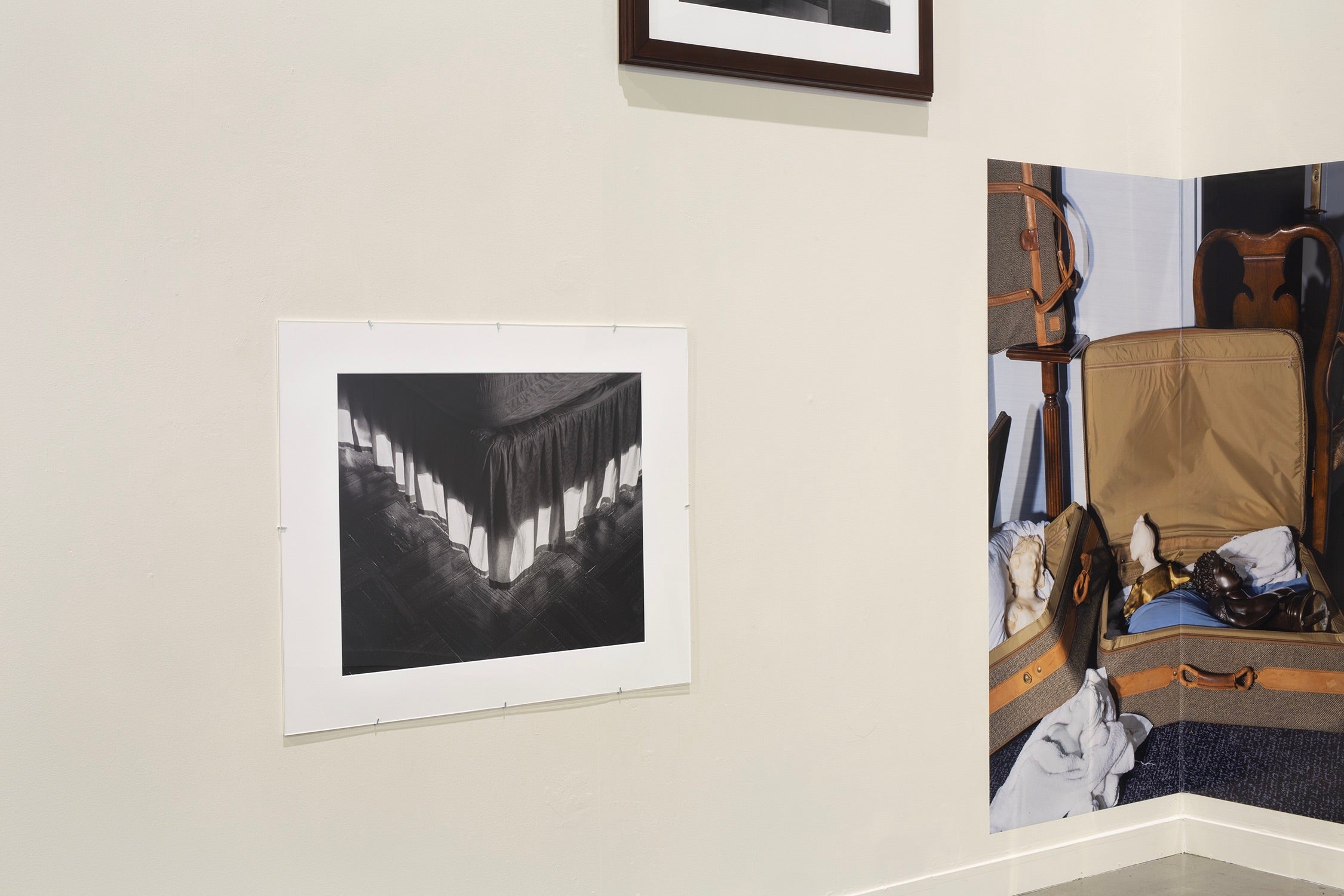 Arrangement of three photographs, one of a bed skirt mounted under a mat board and plexiglass, another color pigment print mounted in a corner, the third barely visible above.