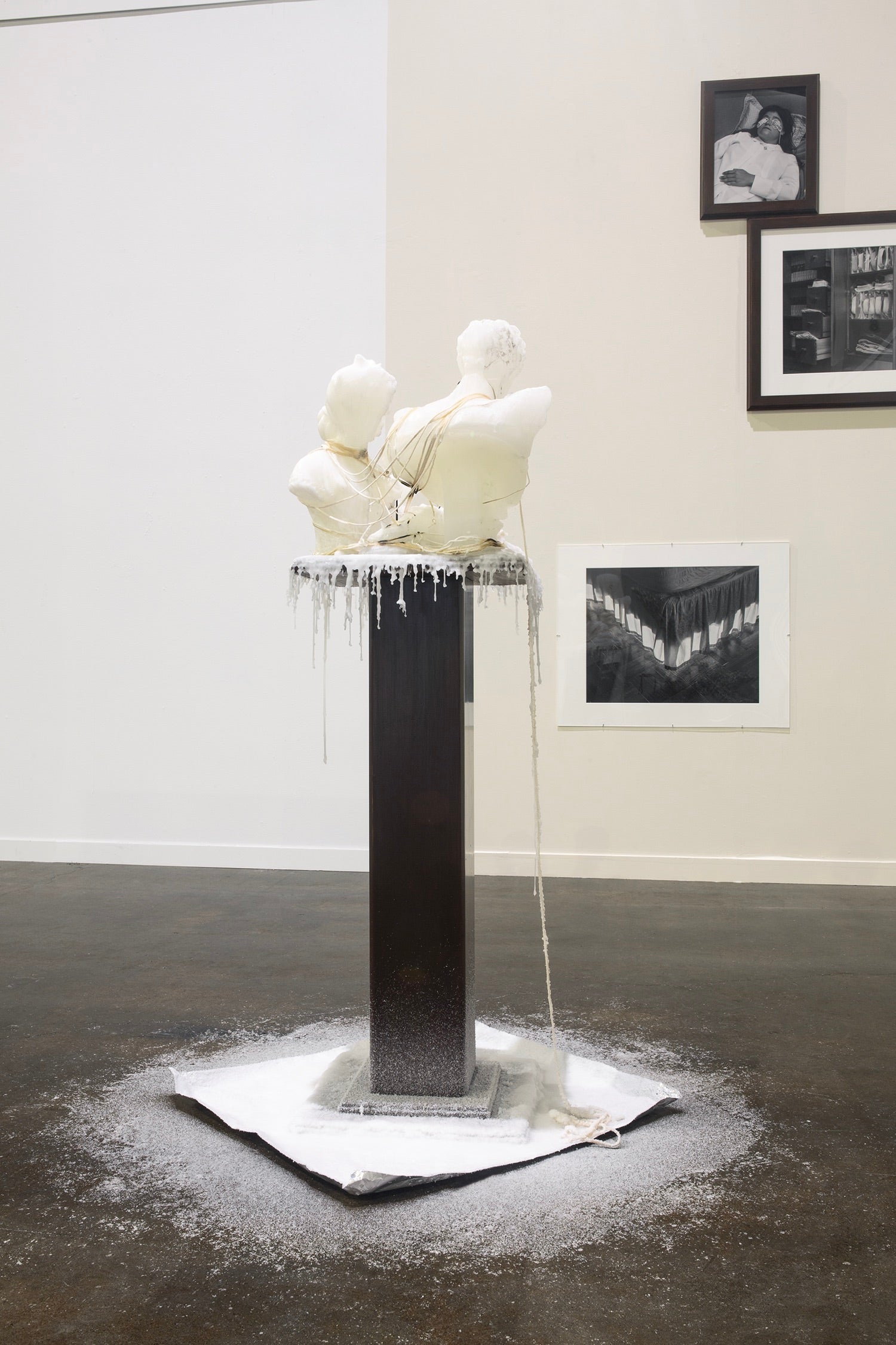 Wax sculpture on wooden podium with wax dripping from figures.