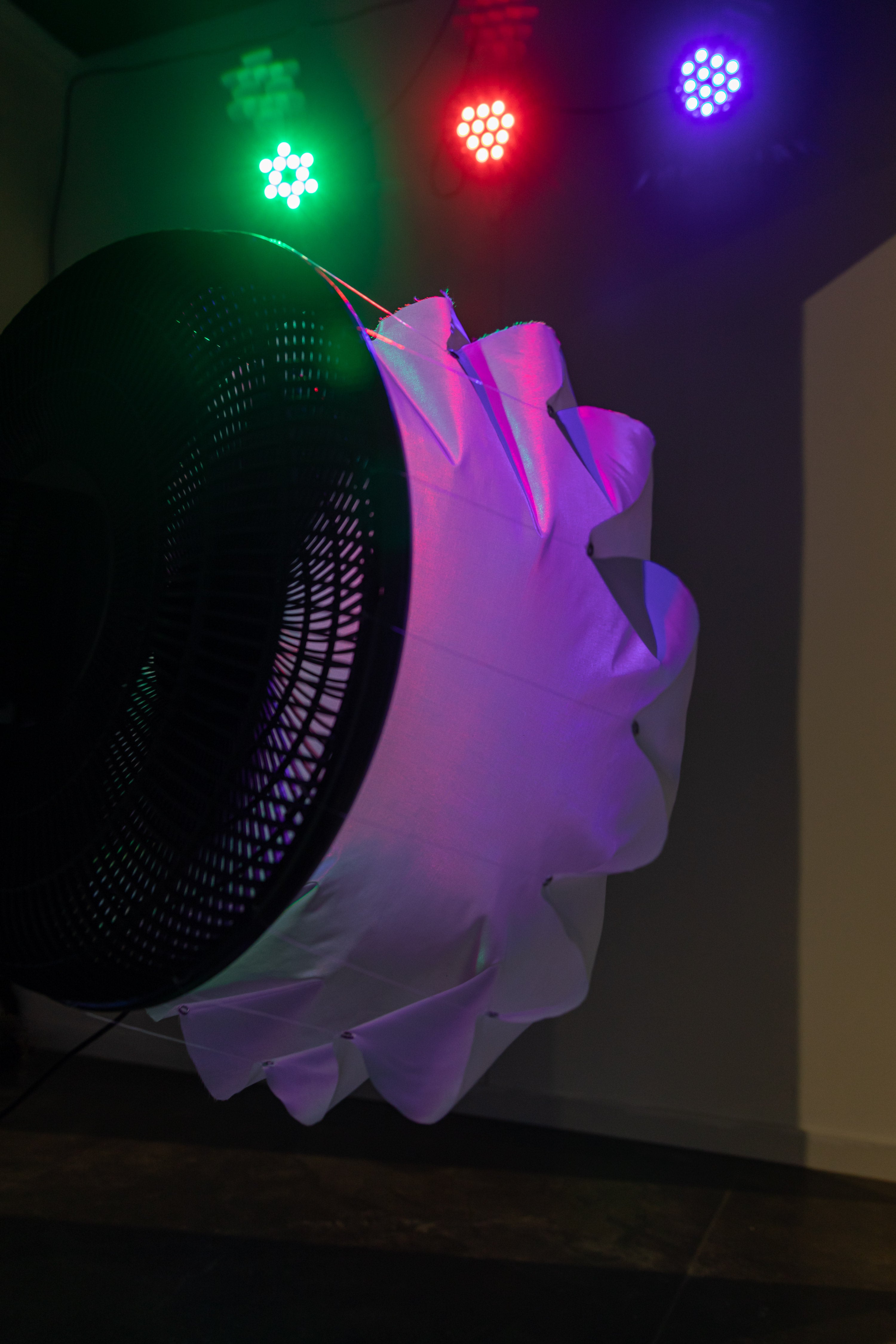 Side view of fan blowing on white fabric, with a small camera attached to the fan