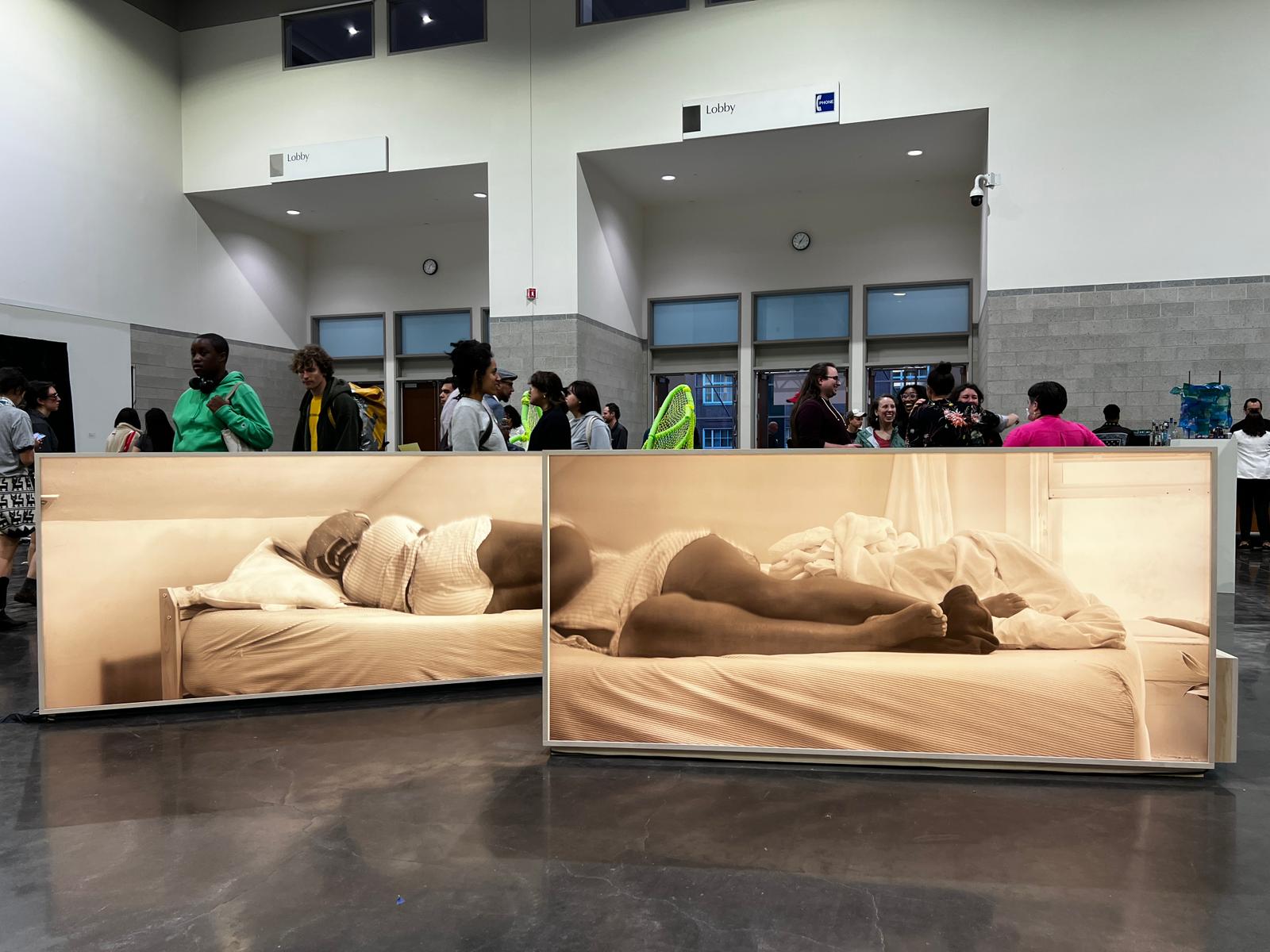 two large horizonal light boxes lit on both sides. one side has a silhouetted body making repeated gestures and the other in a person laying in a bed