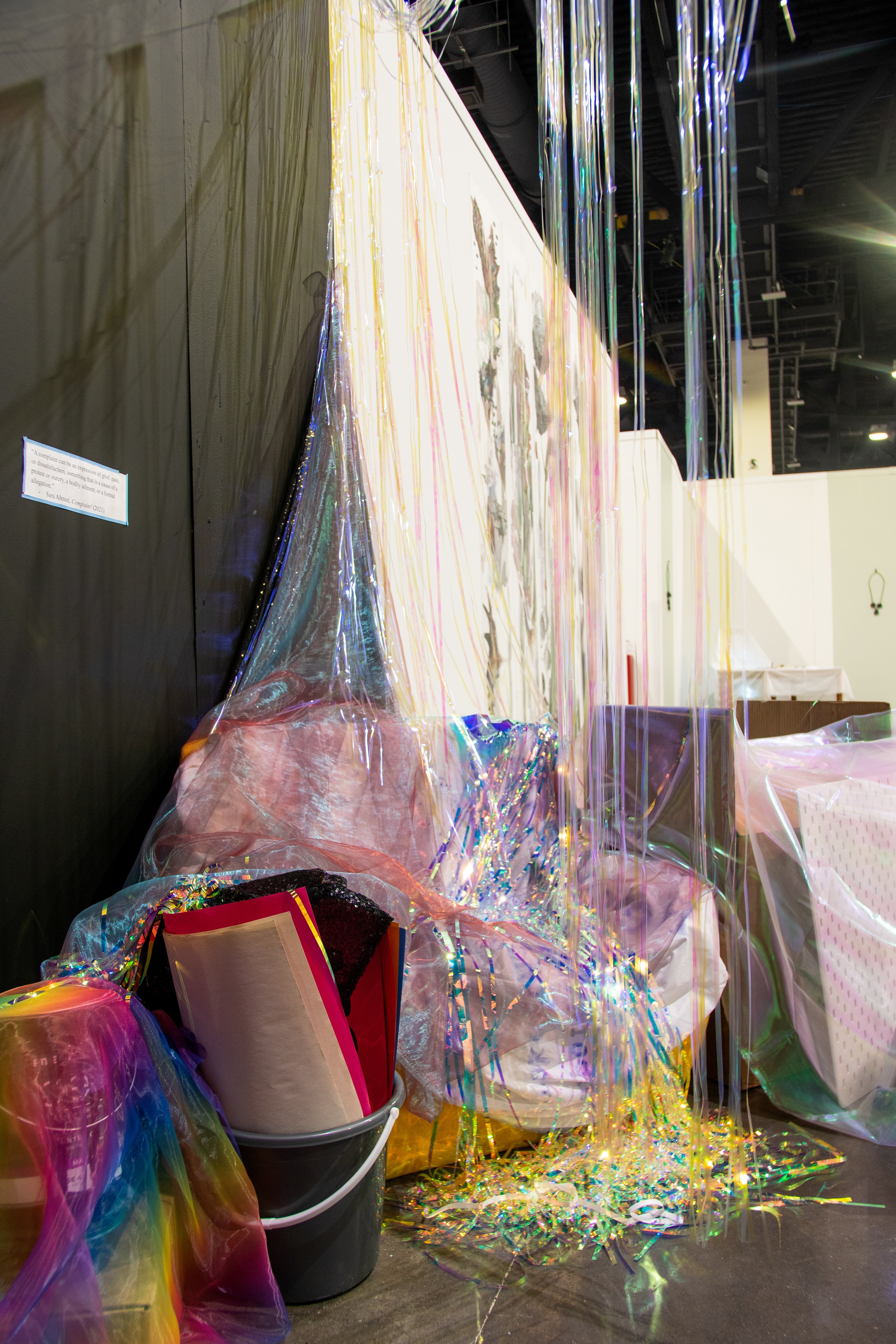 iridescent vinyl streamers hanging from above to ground; bucket filled with posters; belongings covered with fabric