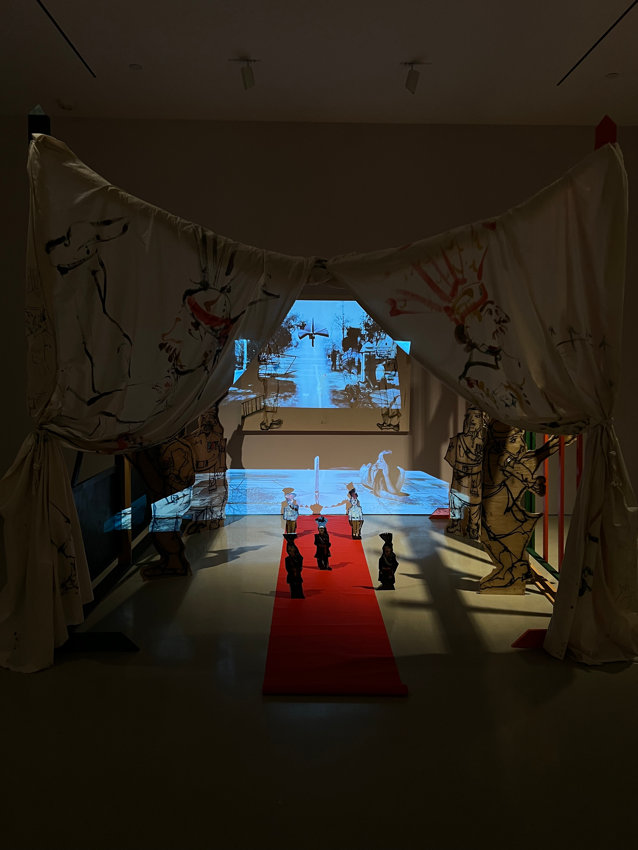 installation comprising oil painting on canvas, masonite, and muslin; charcoal and found fabric on wood cutouts, wooden handmade gates, sound, video performance (05:22), projection, carpet, and hardware