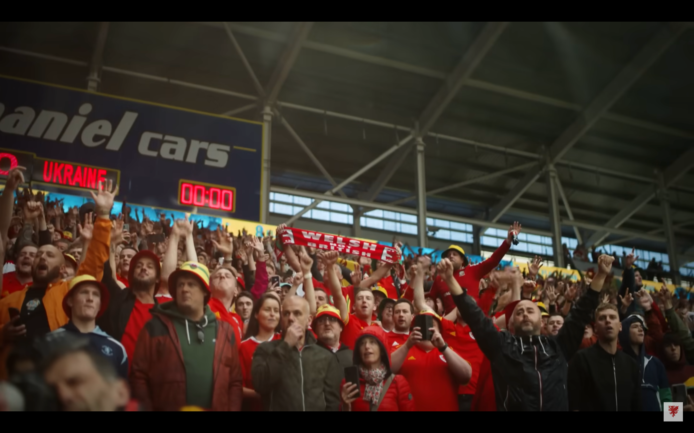 A Welsh football fan in a crowd holding a scarf with the words "WELSH NOT BRITISH."