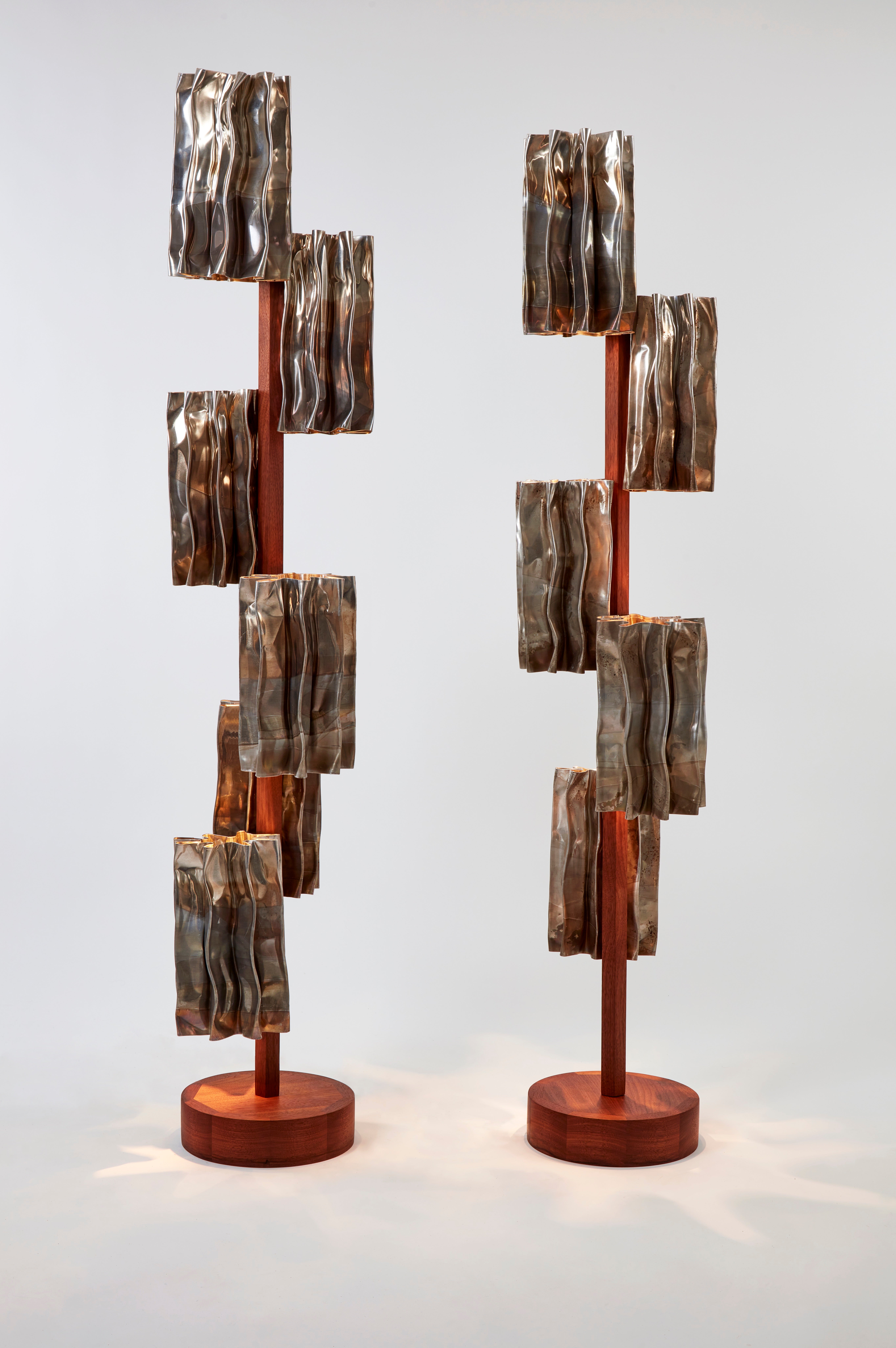 Two modern floor lamps display similarly styled metallic aluminum segments as decorative shades with a central walnut pole and base.