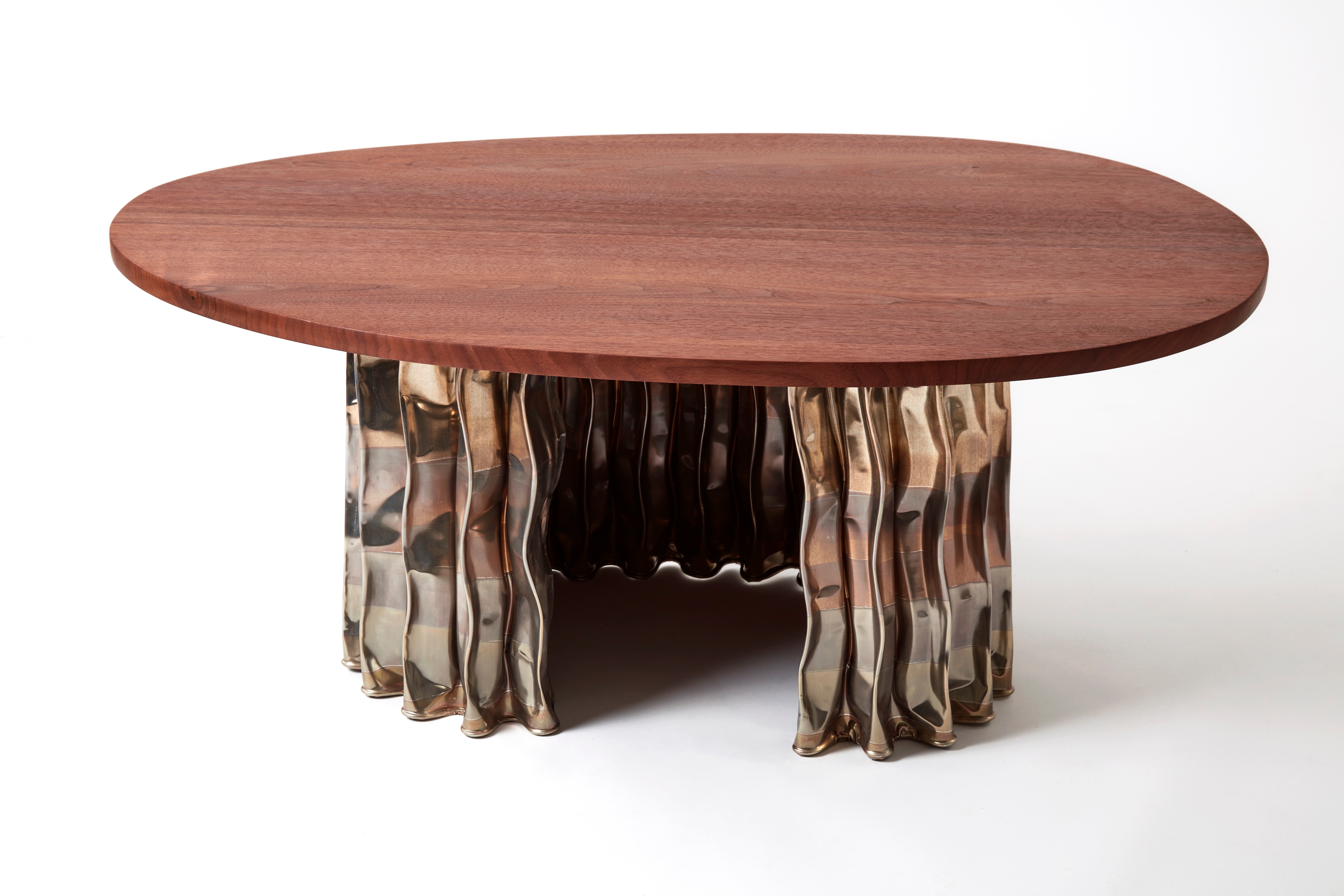 A round coffee table with a smooth walnut top and a unique, wavy metallic base. The base features a reflective surface with an elegant, flowing design, creating an artistic contrast with the wooden tabletop.
