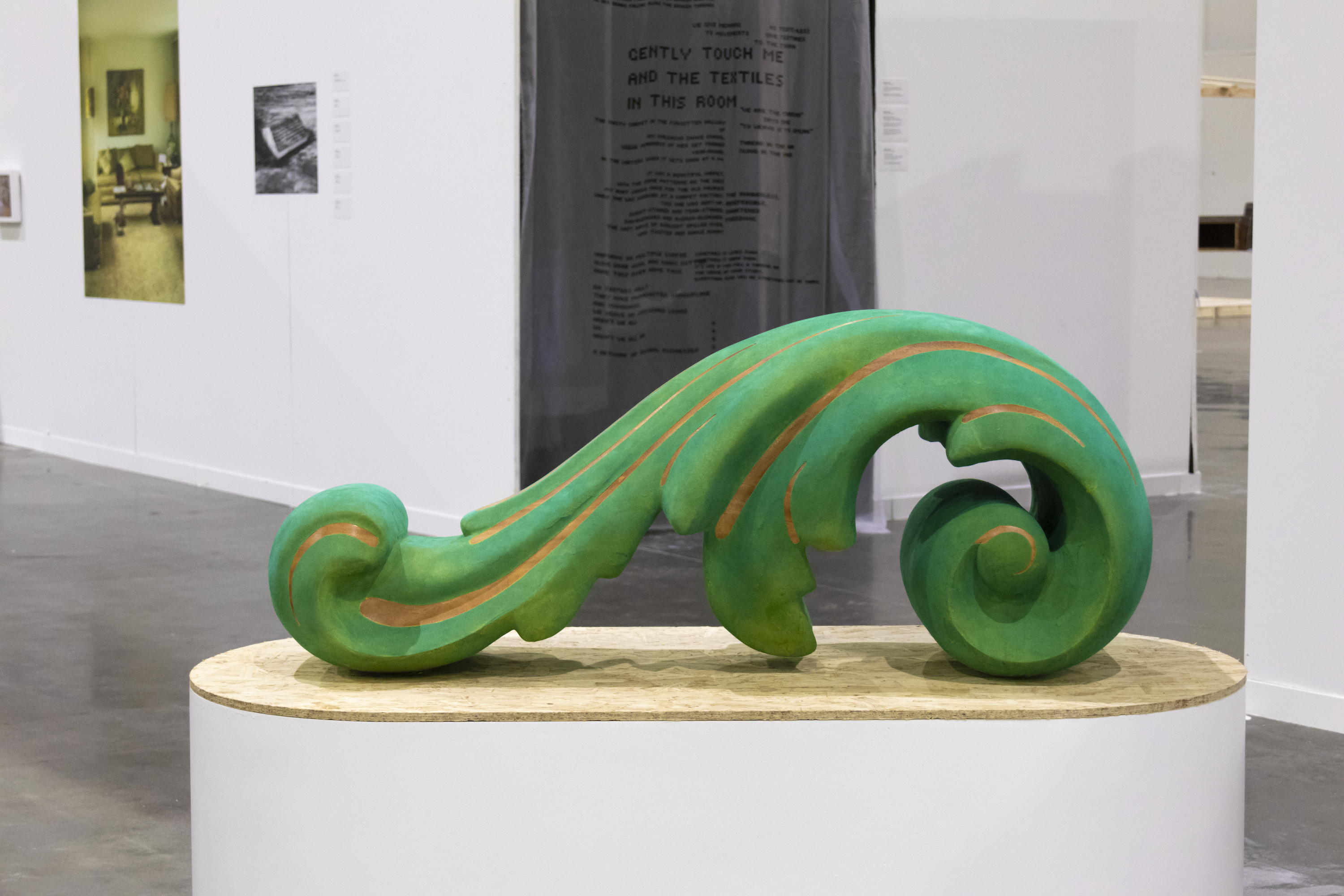 A large green acanthus ornament sits on a high pill-shaped plinth with an Oriented Strand Board top surface.