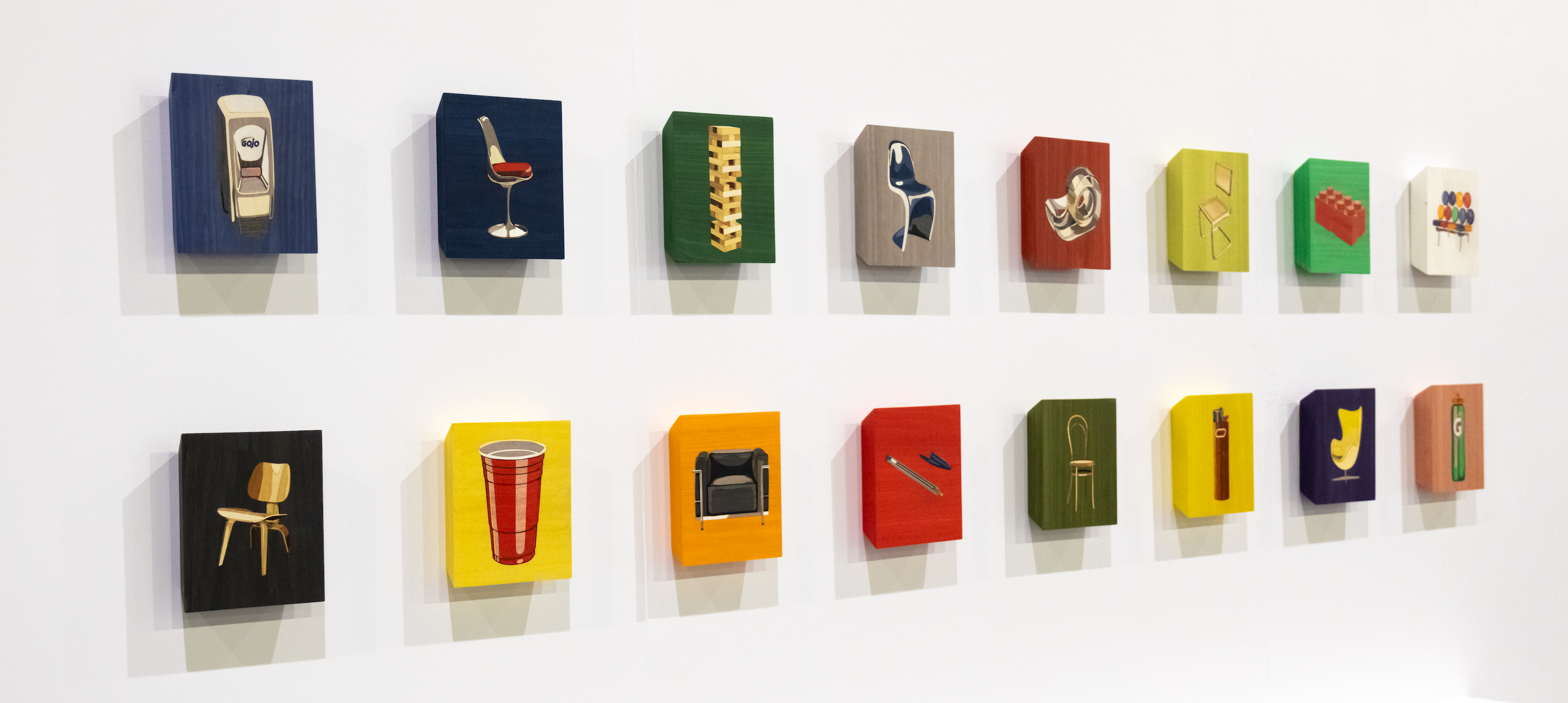 16 square panels on a wall in a 2-row grid viewed at a slight side-angle. Each depicts an iconic mid-century chair or a cheap ubiquitous product. Each has a different colorful background.
