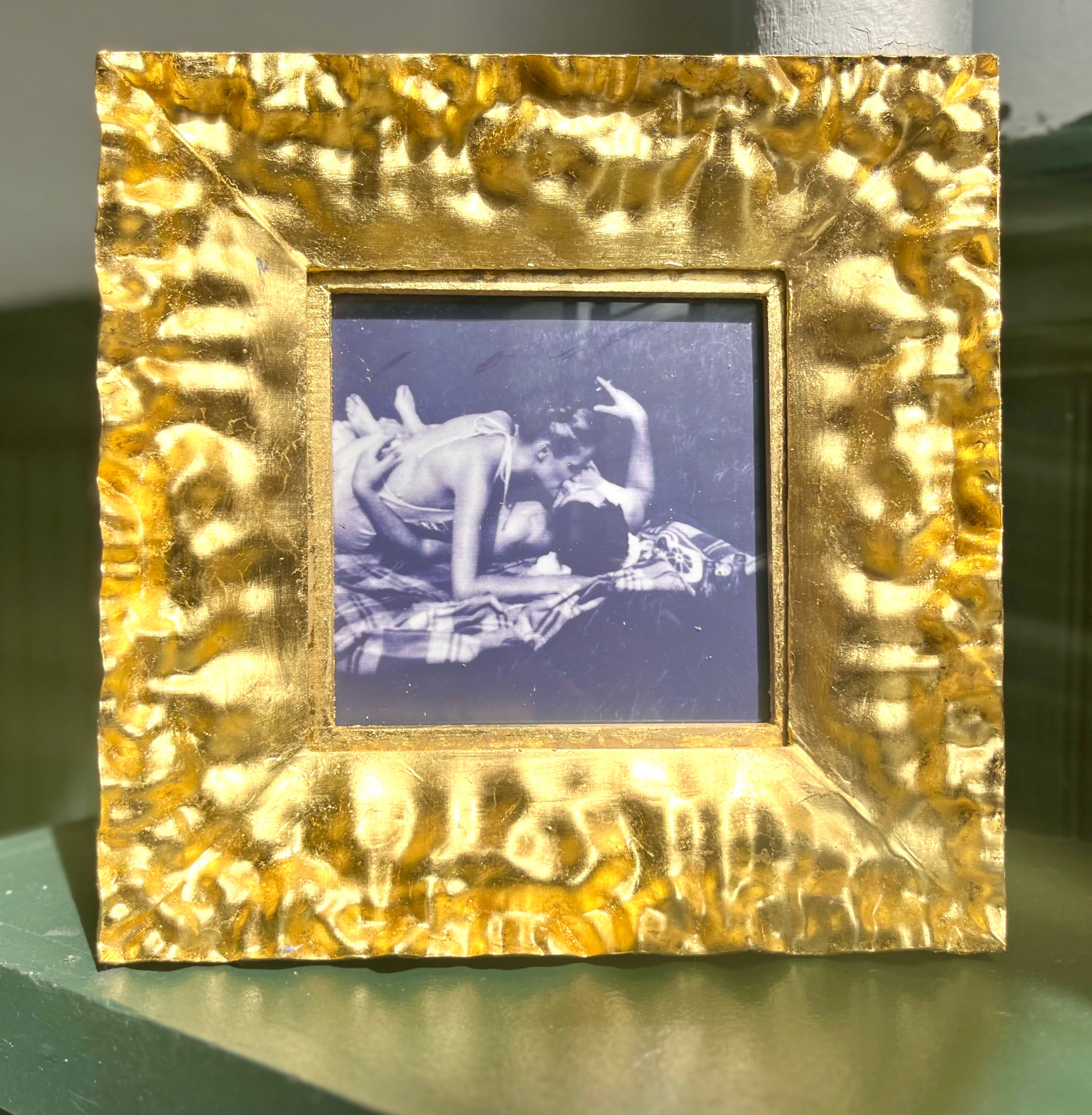/A%20golden%20frame%20holds%20a%20black-and-white%20vintage%20photo%20of%20two%20people%20kissing%20on%20a%20blanket%20in%20the%20park.%20