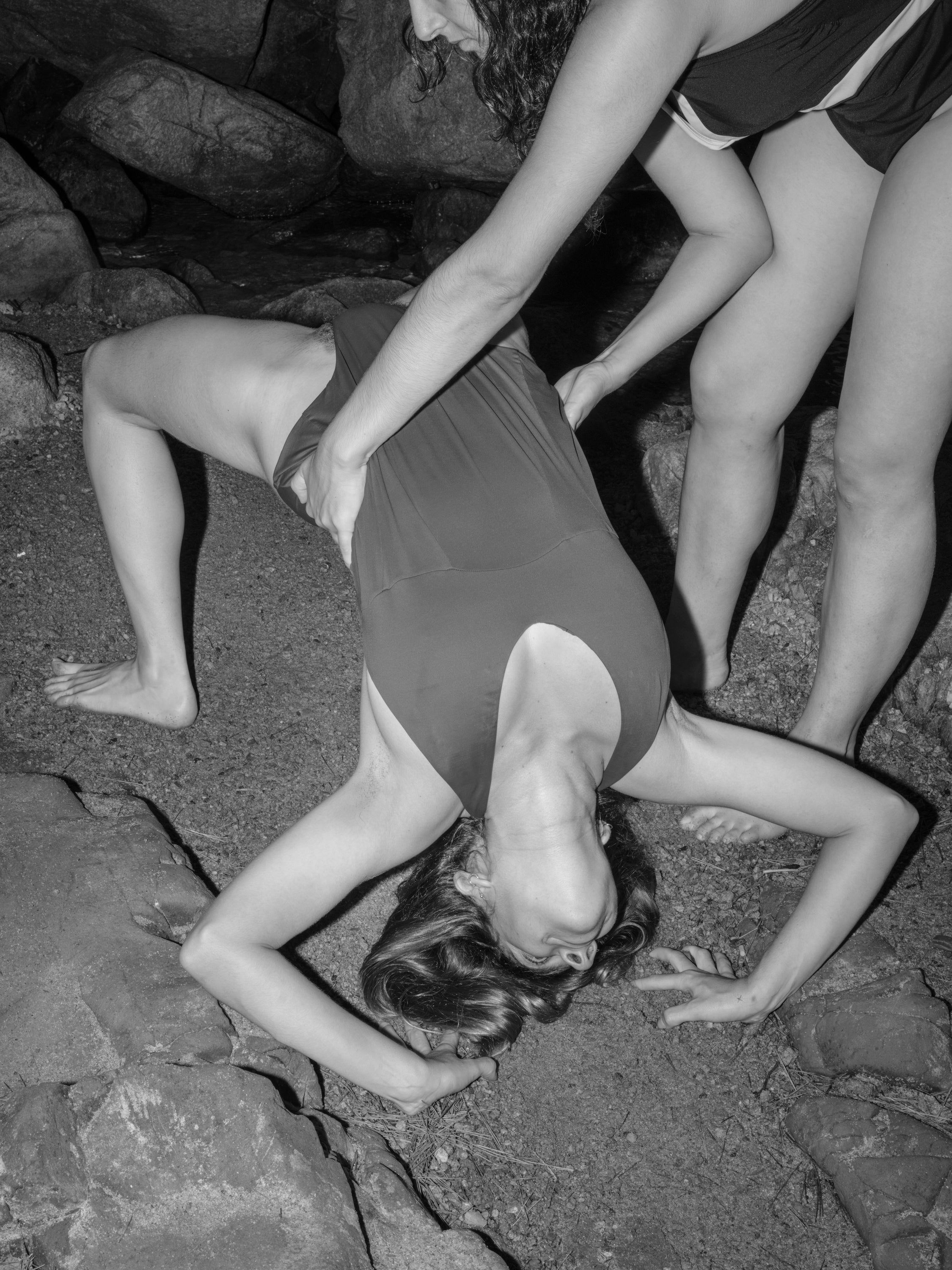 /Black%20and%20white%20photograph%20of%20two%20people%20on%20the%20rocks%20of%20a%20beach%2C%20one%20person%20holding%20the%20other%20while%20she%20tries%20to%20make%20a%20complicated%20body%20posture