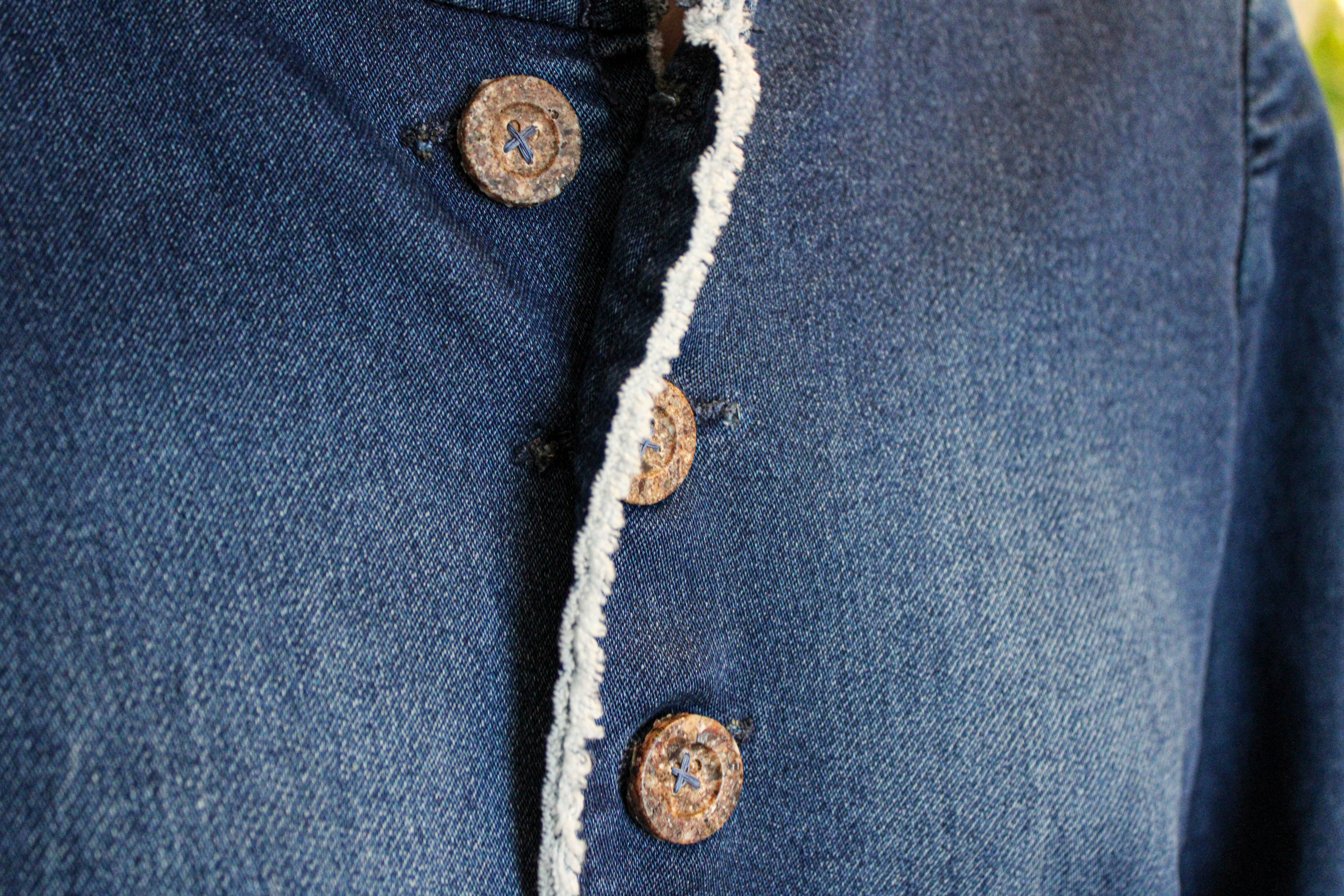 A close-up shot of three buttons made of periwinkle shells ground up and casted back together into the shape of a traditional button. They are stitched with blue thread onto a denim jacket.
