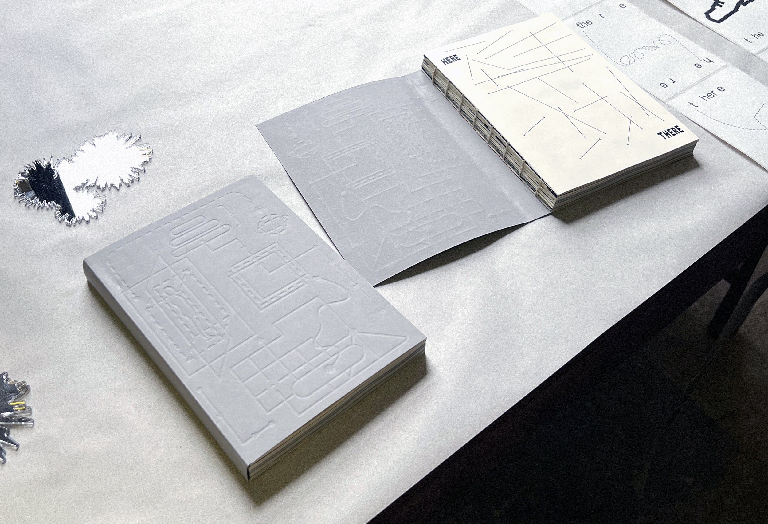 /A%20desk%20with%20two%20grey%20books%20on%20it%20The%20cover%20of%20the%20book%20is%20a%20debossed%20illustration%20of%20lines%20and%20arrows.