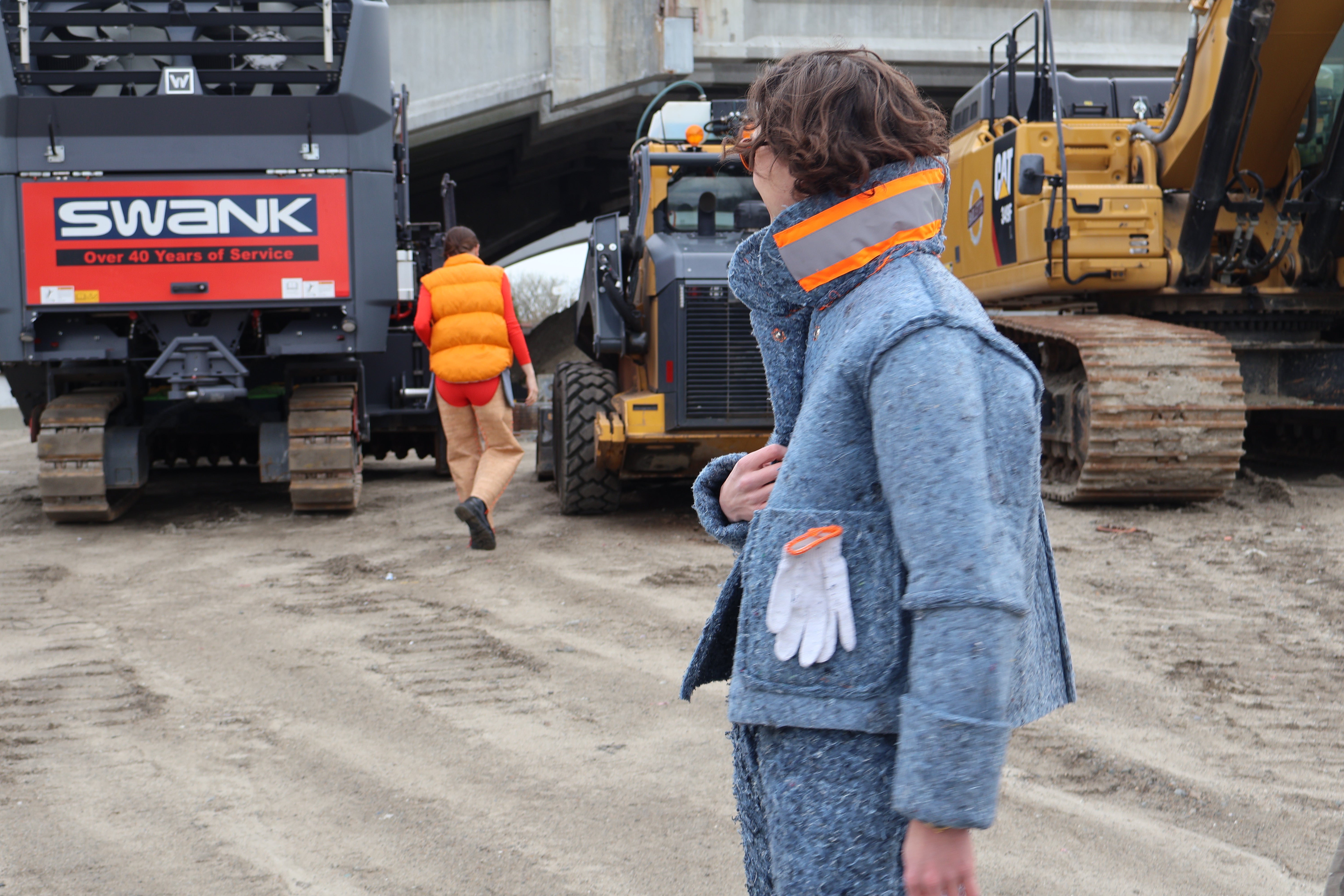 /Photograph%20of%20two%20people%2C%20one%20in%20the%20foreground%20wearing%20the%20Denim%20Insulation%20Suit%2C%20the%20other%20person%20is%20walking%20away%2C%20wearing%20the%20orange%20Shoddy%20Vest%20and%20Cork%20Chaps.