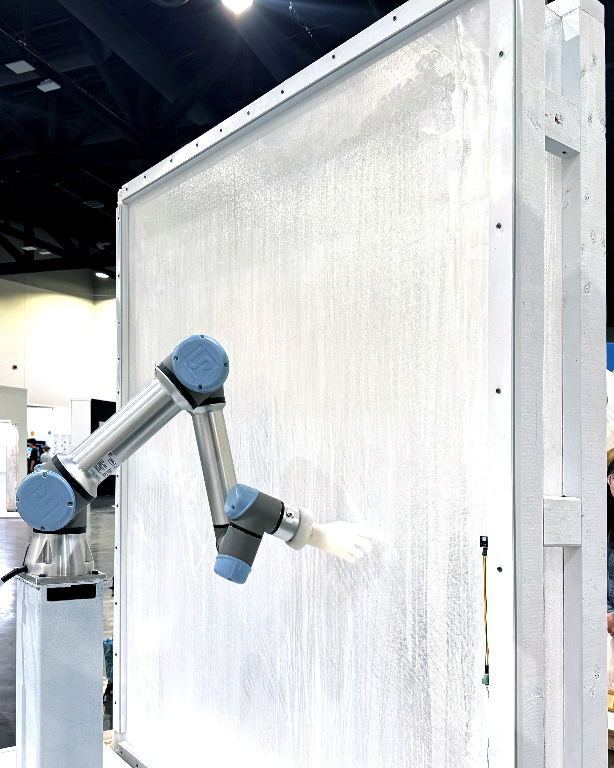 A robotic arm with white silicone hand, grazing a semi-translucent membrane with its index finger.