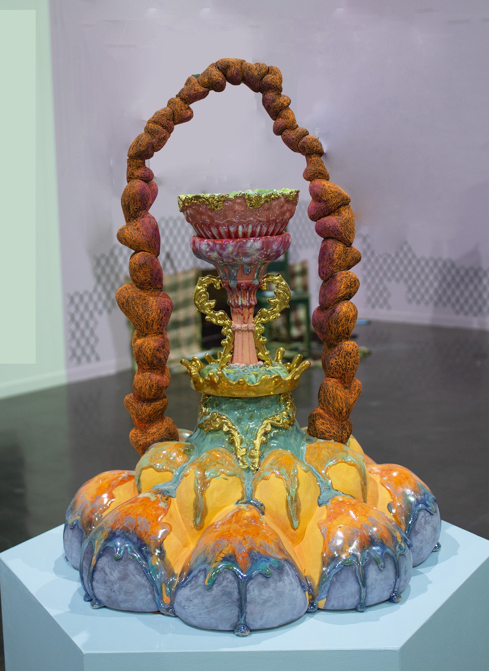 An elaborate ceramic sculpture with vibrant orange, blue, and gold hues, featuring drip-like textures and intricate details. It is an abstract form of flower. 