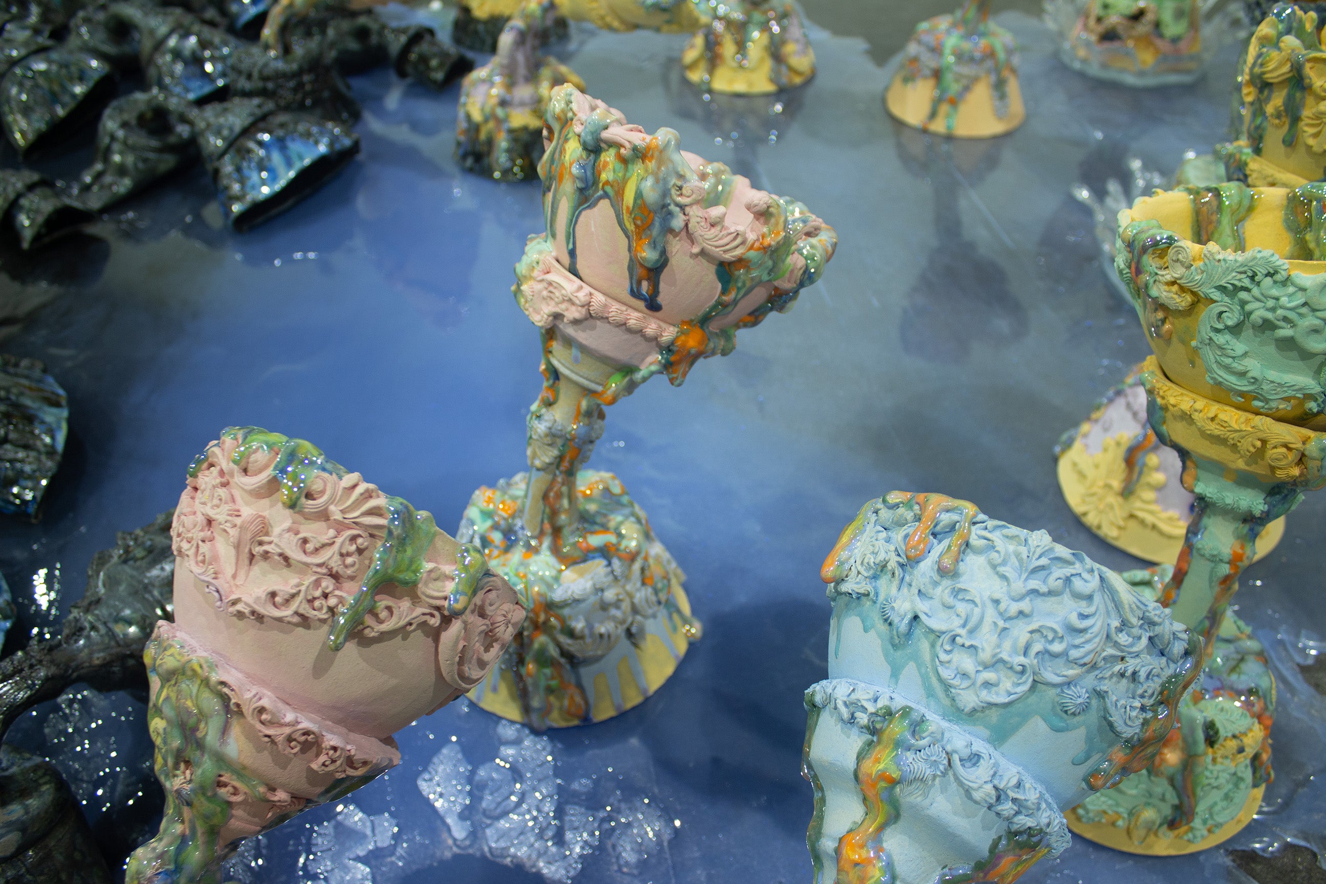 /Close-up%20of%20intricately%20decorated%20the%20Holy%20grail%20with%20dripping%20glazed%20surfaces%20and%20covered%20with%20pastel%20colors%2C%20standing%20on%20a%20glossy%20blue%20reflective%20surface%20which%20is%20water.