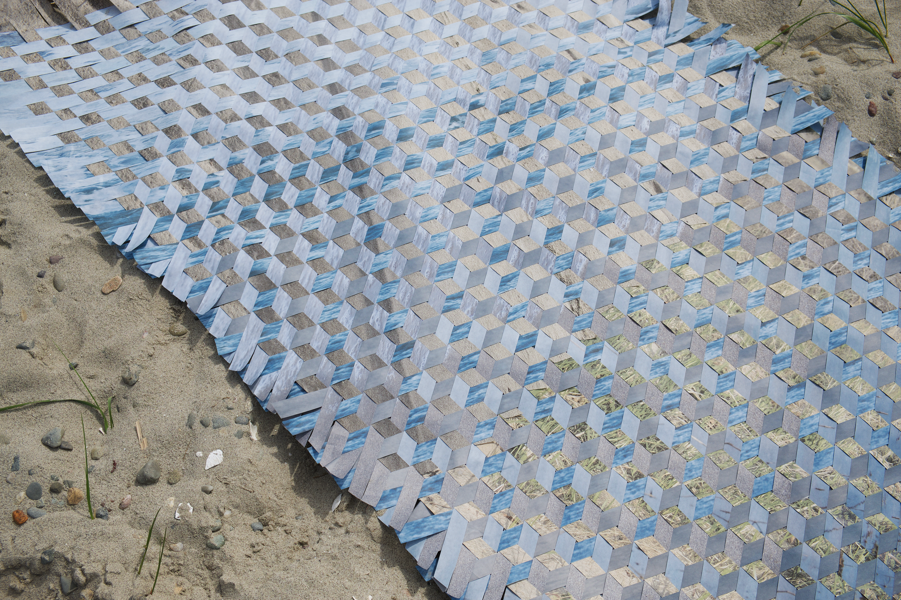 /Woven%20photographs%20on%20paper%20displayed%20on%20sand.