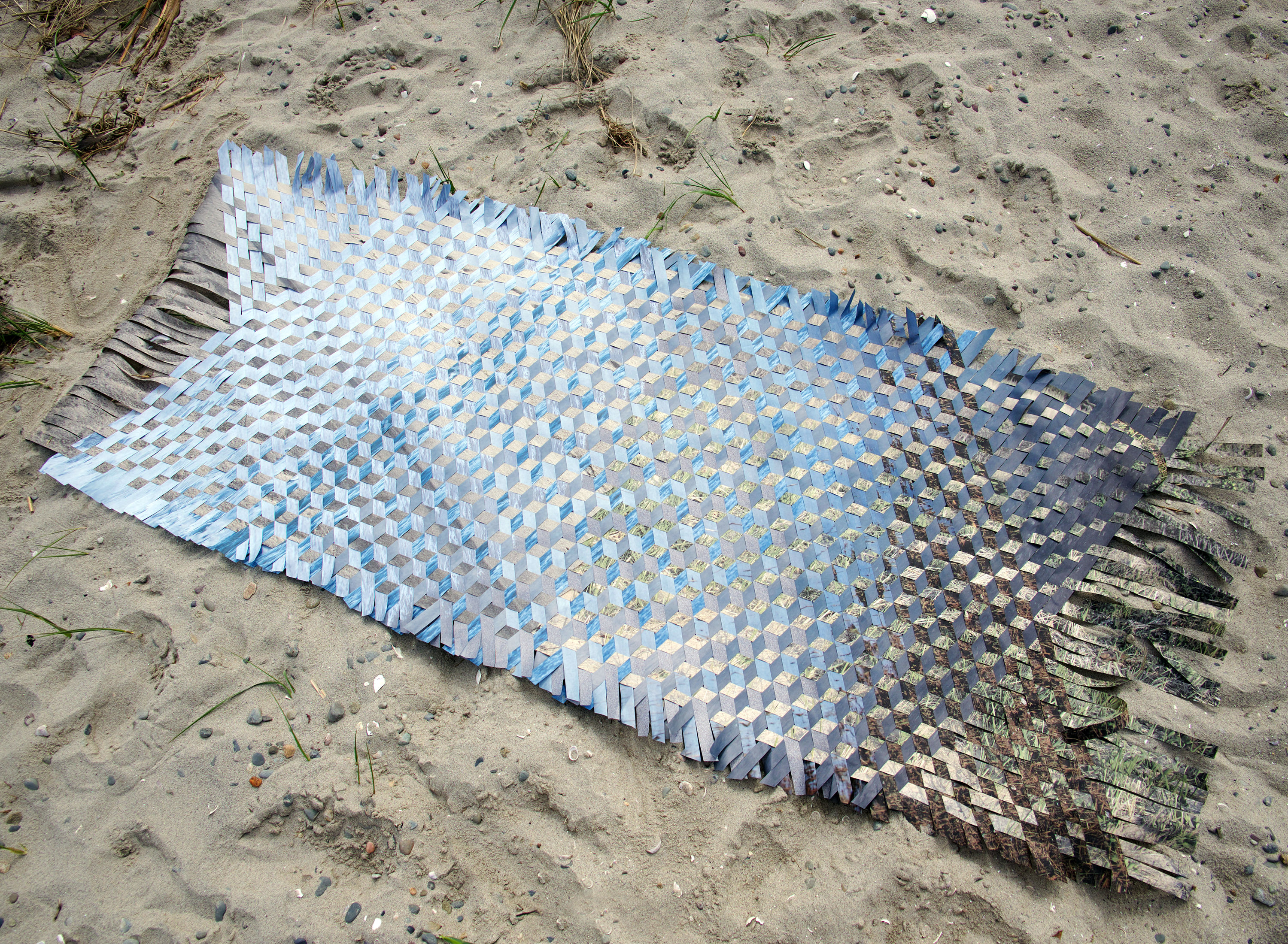 /Woven%20photographs%20on%20paper%20displayed%20on%20sand.